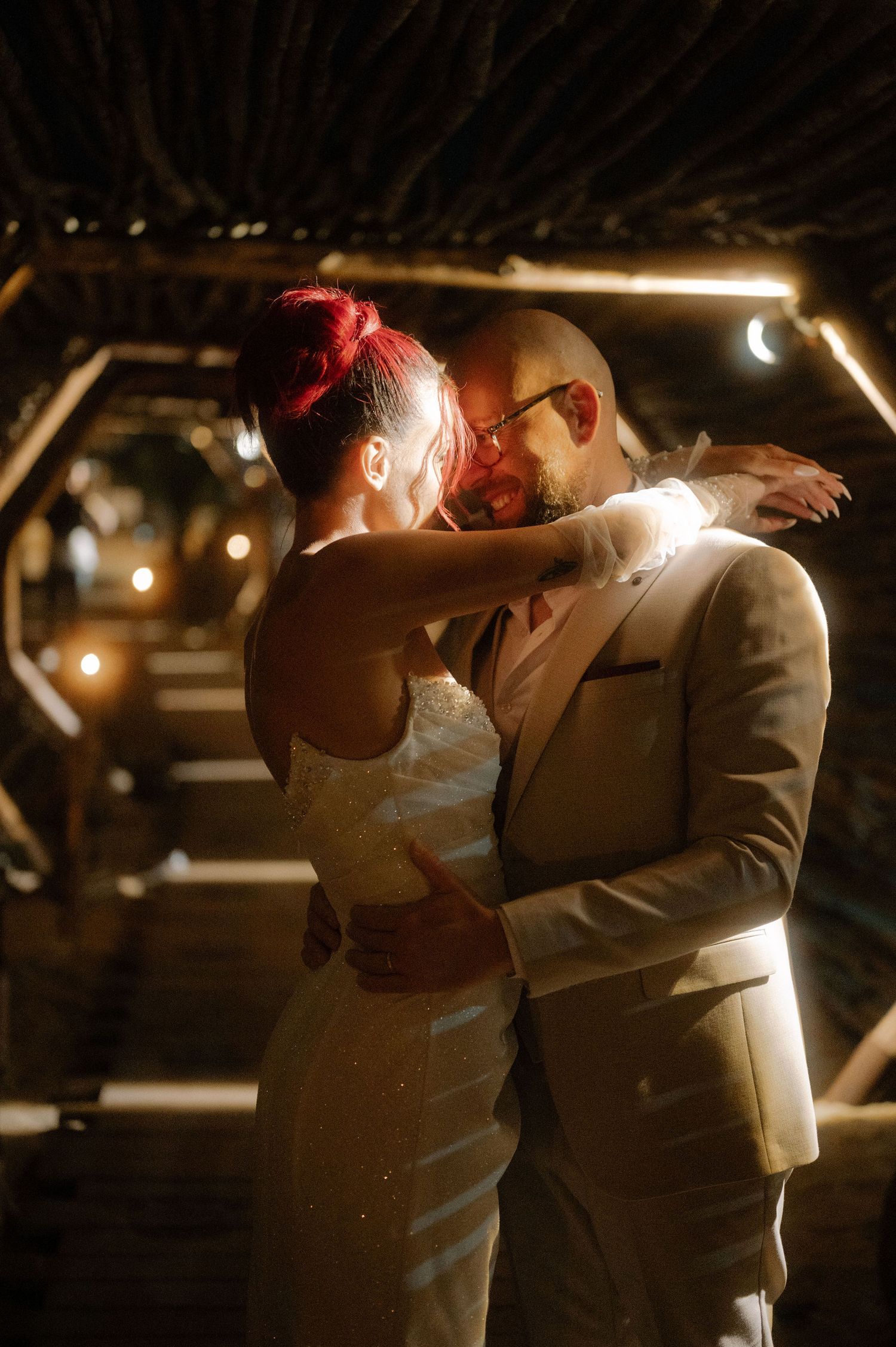 A couple shares a romantic dance together in dim lighting at an evening reception.