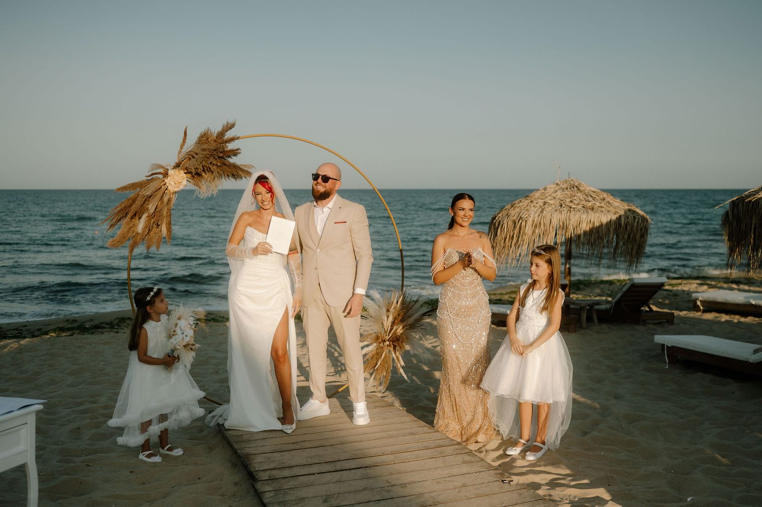 Wedding party walks along scenic beach boardwalk at sunset with ocean waves crashing in background.