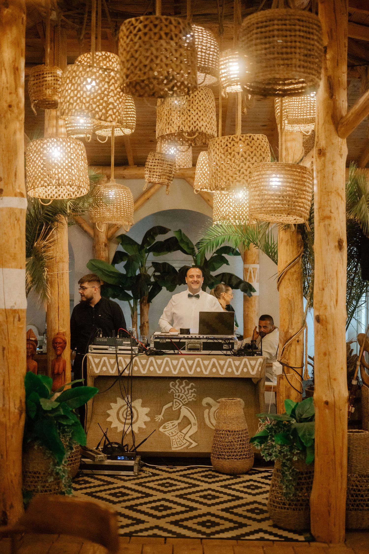 Rustic restaurant interior with woven bamboo pendant lights, wooden beams, and tropical plants creating a warm ambiance.