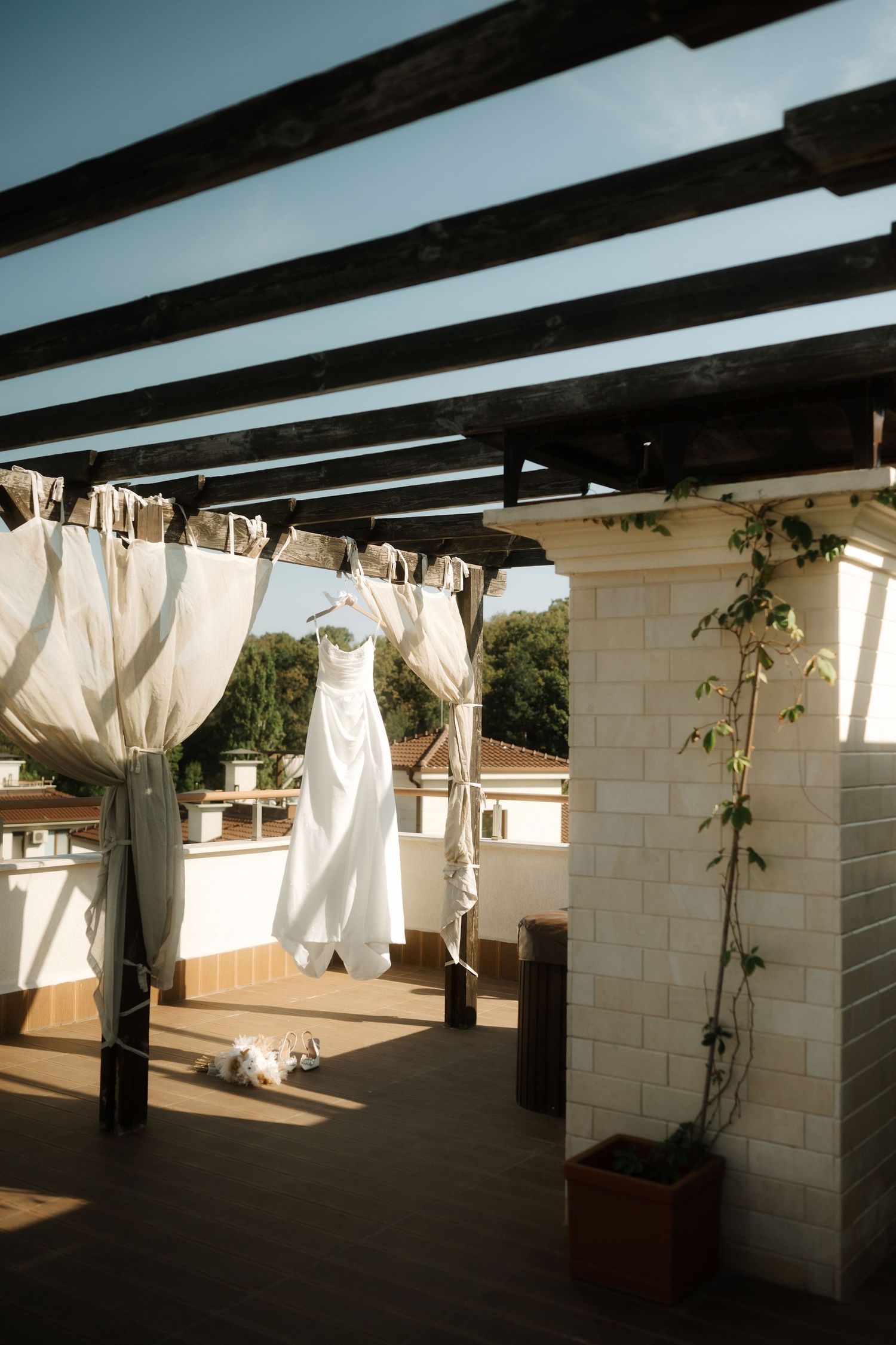 White curtains blow gently in the breeze along a covered outdoor patio with stone columns and wooden beams.