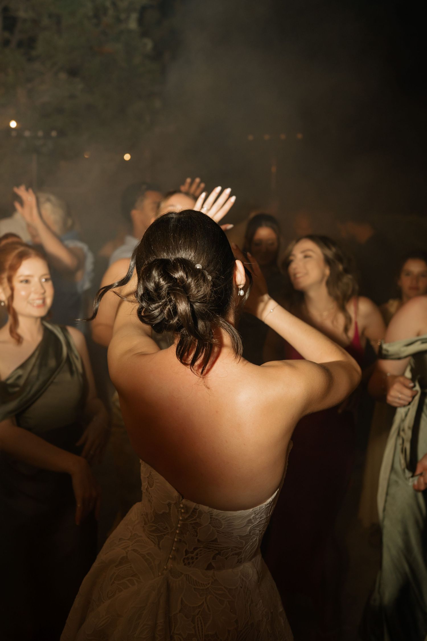 Bride in lace wedding gown dancing with guests at a smoky wedding reception celebration.