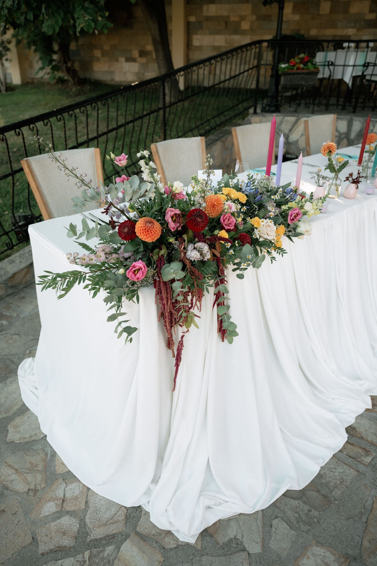 White tablecloth adorned with cascading floral arrangements featuring pink, orange and burgundy blooms with greenery.
