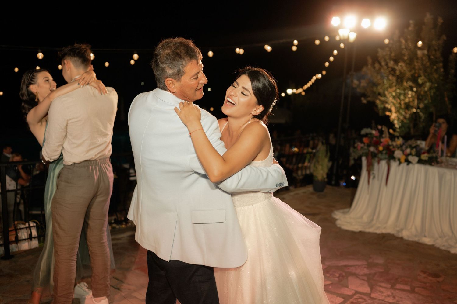 A romantic outdoor evening wedding reception with couples dancing under twinkling lights and decorative lanterns.