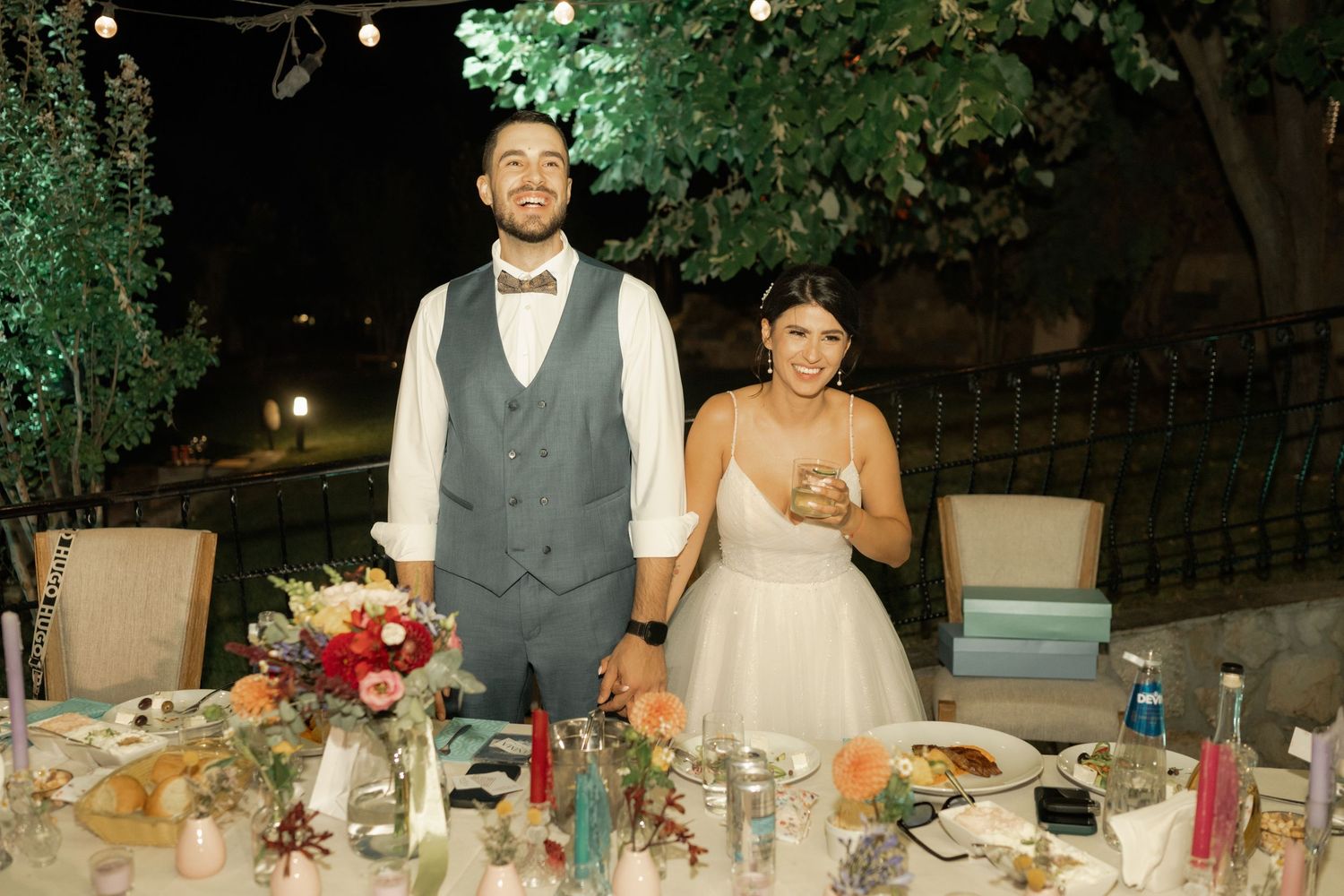 Wedding guests enjoying a festive outdoor reception with string lights and elegant table settings at dusk.