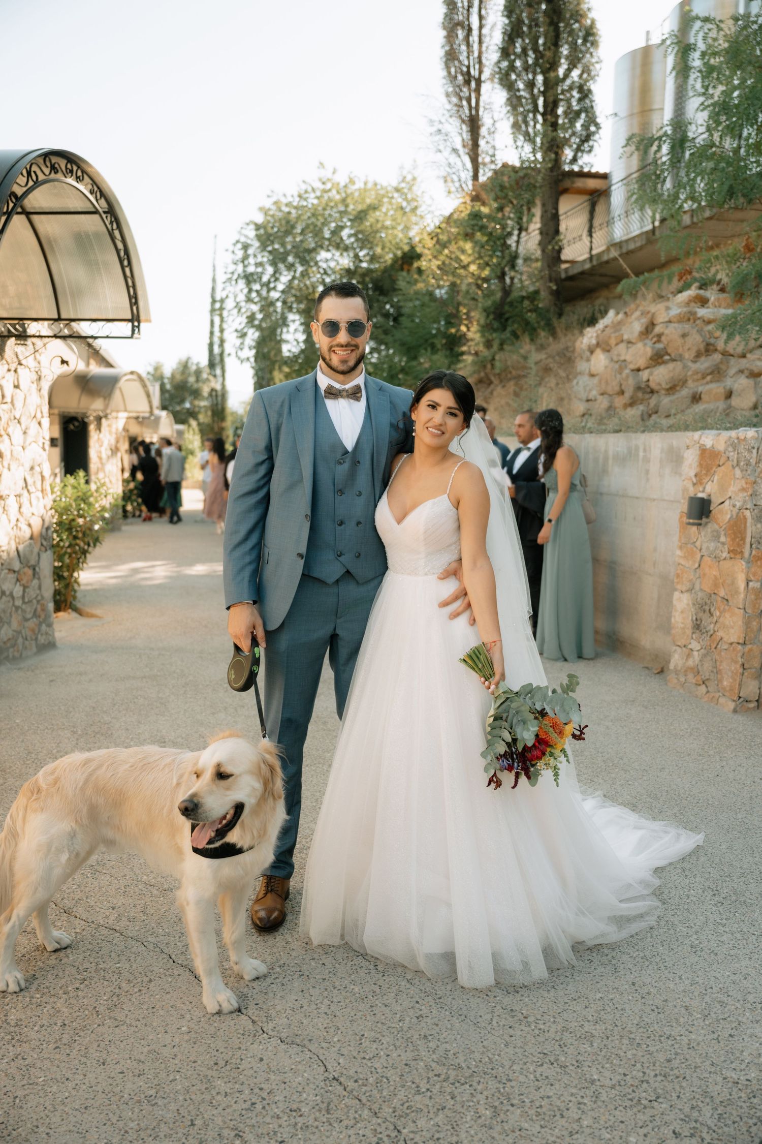 A bride and groom stand with their golden retriever on a rustic stone walkway.