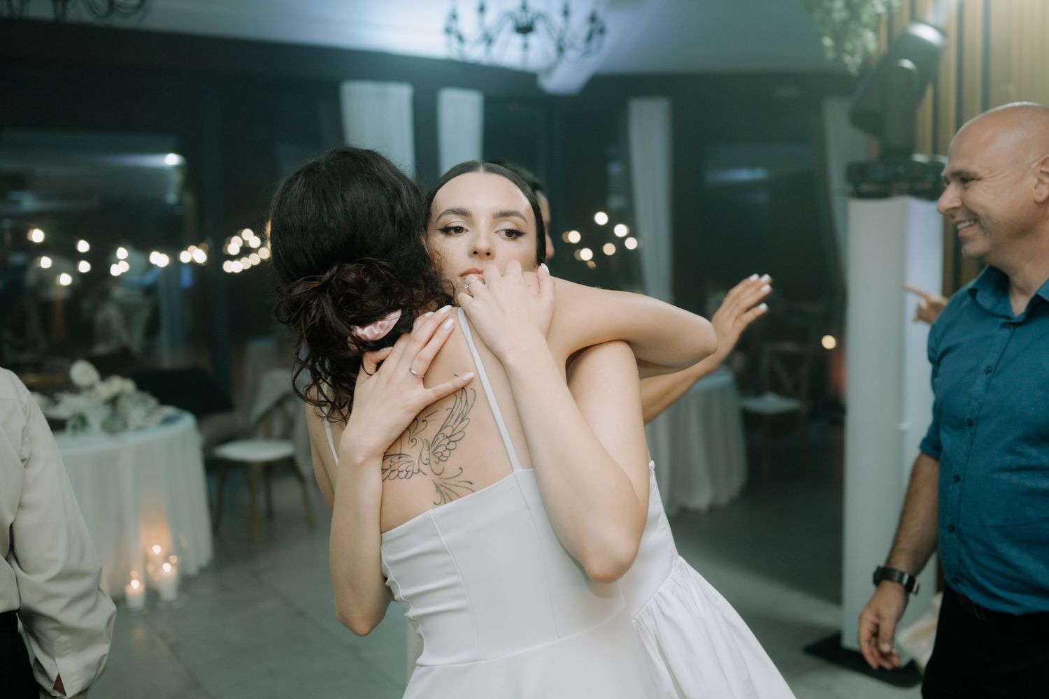 A person in a white dress dances joyfully at what appears to be a wedding reception with string lights in the background.