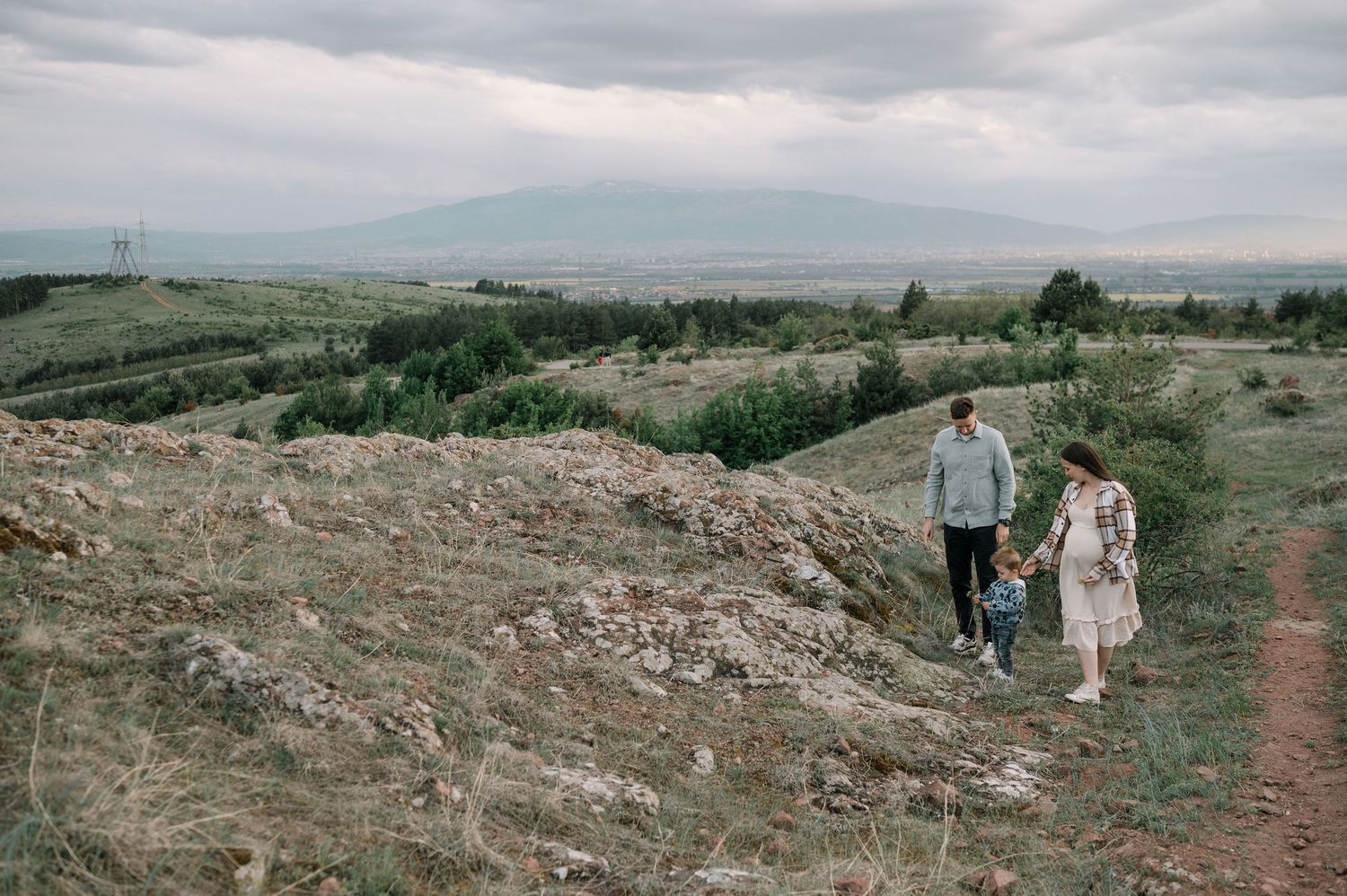 Couples explore a winding dirt path through scenic mountain terrain under overcast skies.