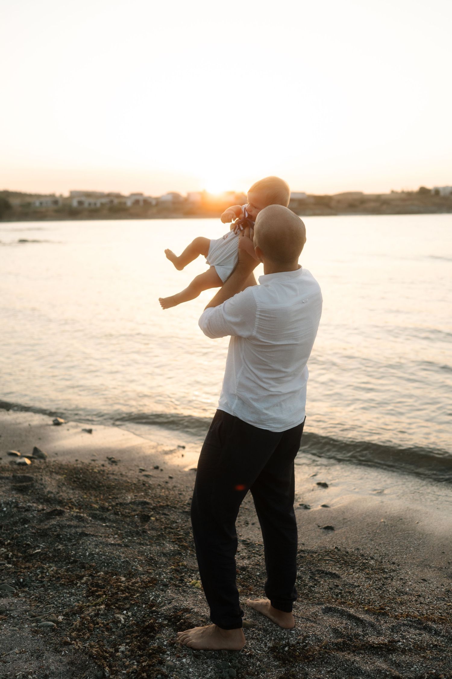 A person in white shirt and dark pants takes photos of sunset at a rocky beach shoreline.
