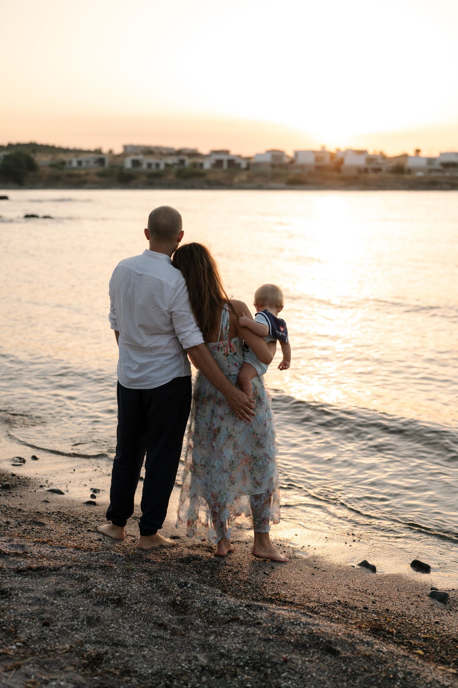 A couple sits together on a rocky beach watching a peaceful sunset over the water.
