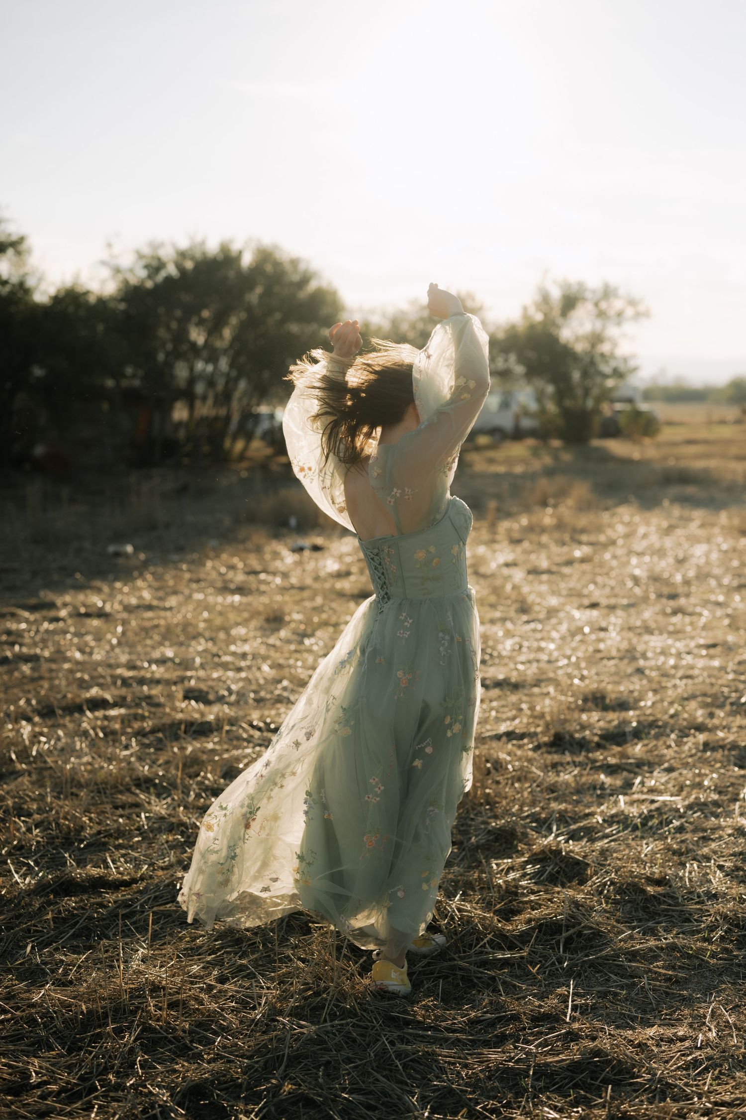 A dreamy figure in a flowing white dress twirls in a sunlit field at golden hour, creating an ethereal silhouette.