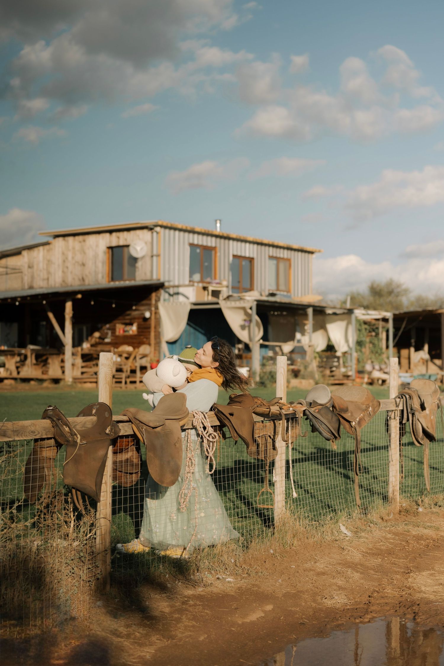 A row of rustic scarecrows stand guard in a rural farm setting against a cloudy sky at sunset.