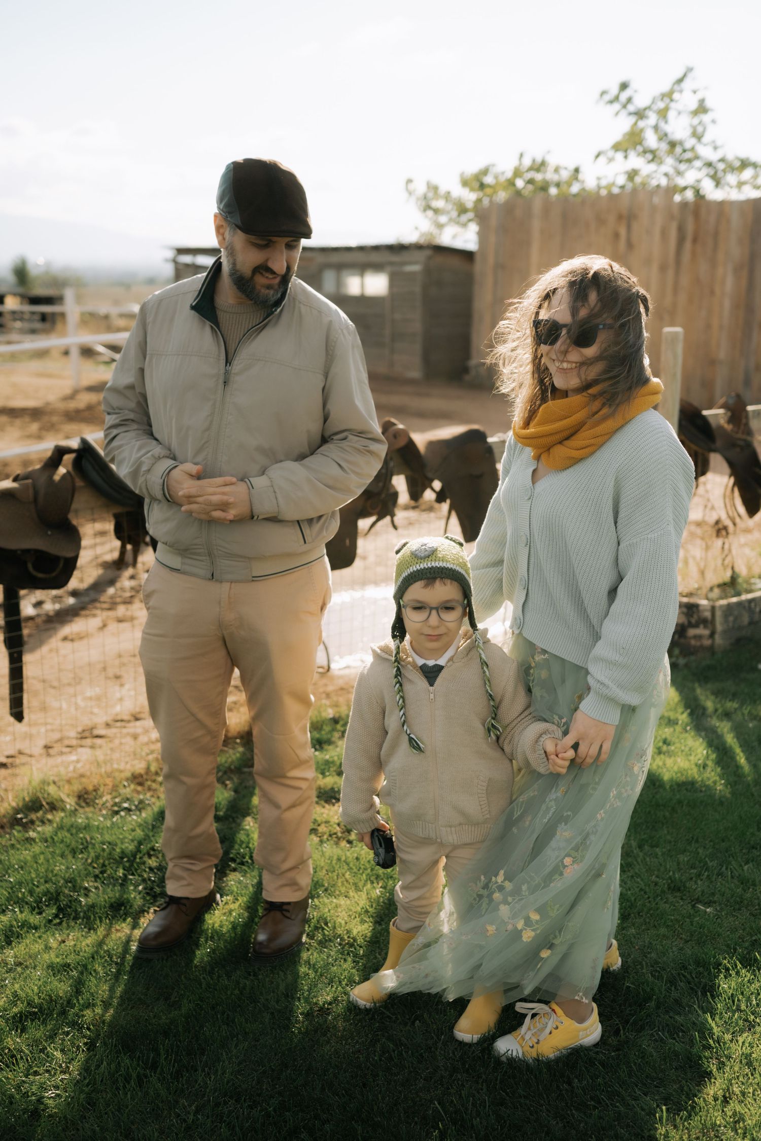 A family in coordinating beige and white outfits holds hands while walking together in a sunny backyard.