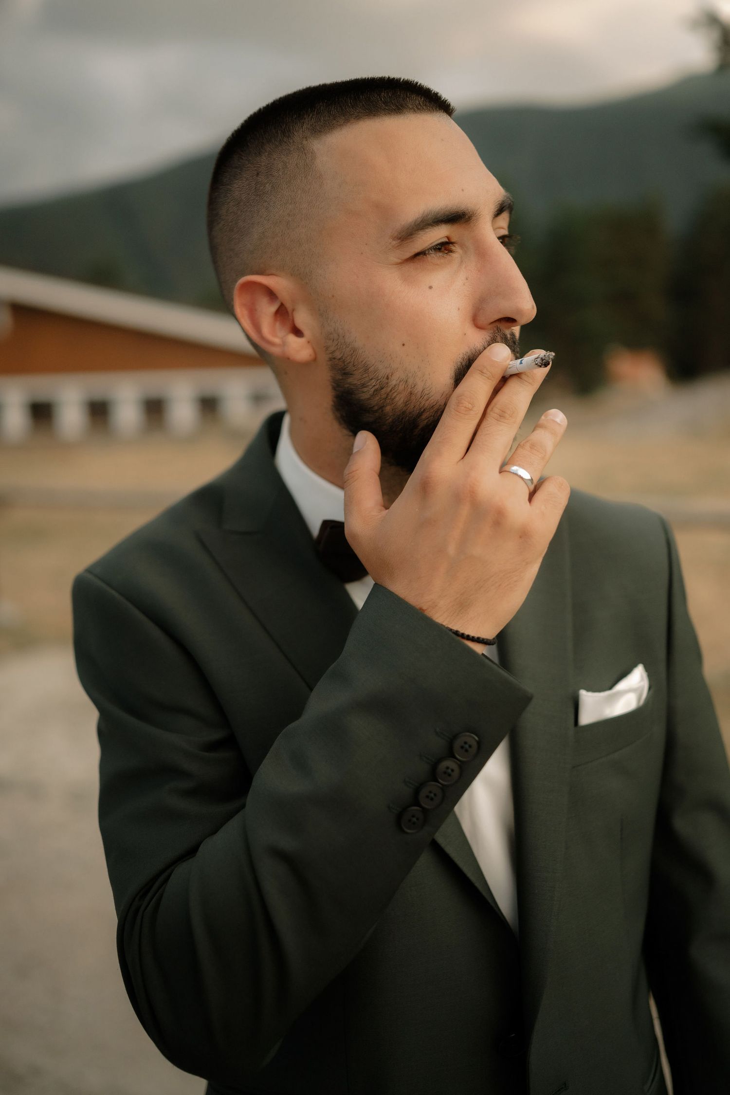 Emotional groom in black suit covers his mouth with his hand while crying during a wedding ceremony.