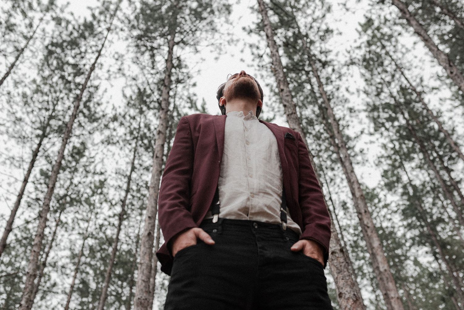 A person in a burgundy blazer and white shirt stands in a snowy forest setting during winter.