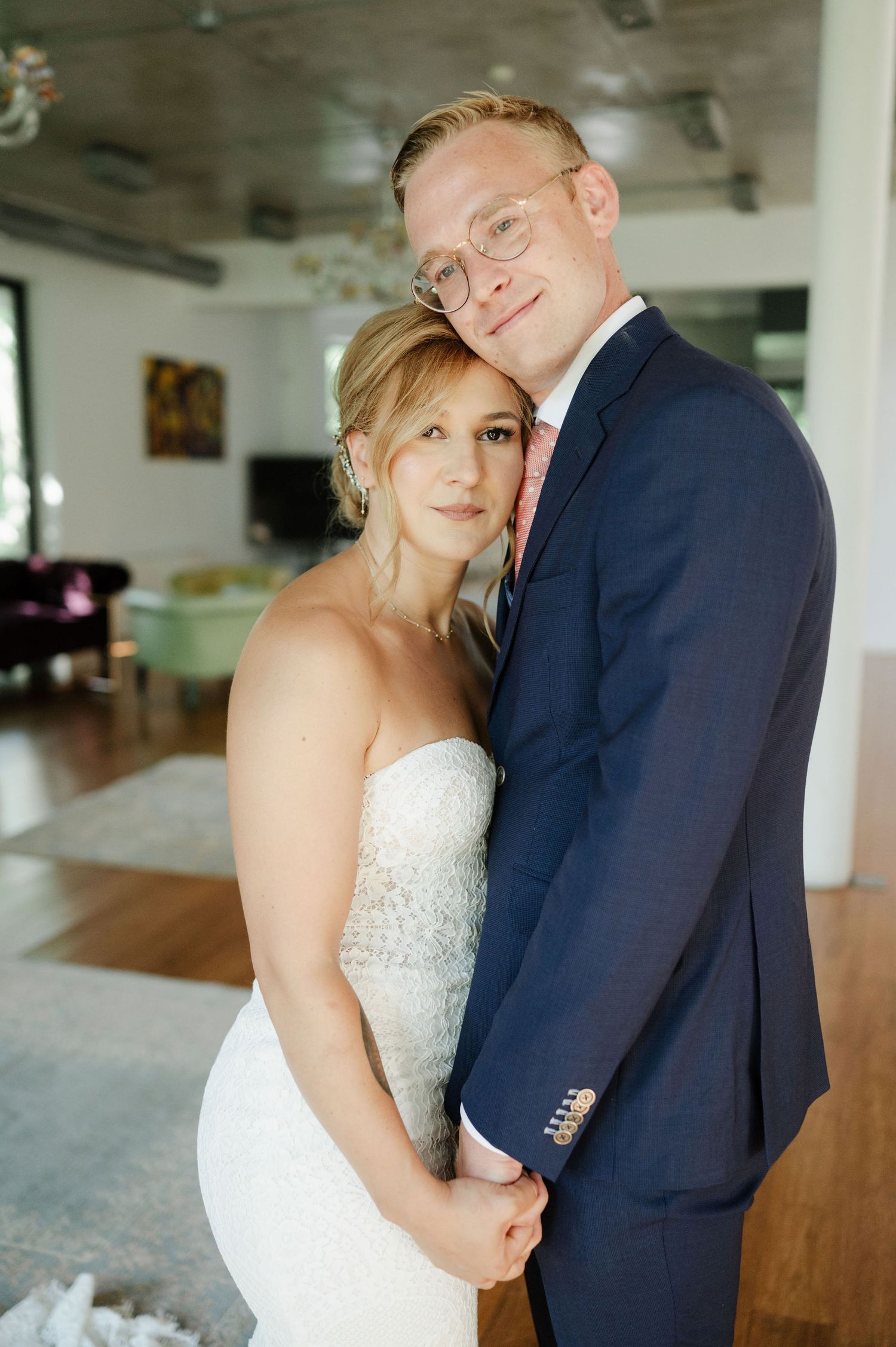 A romantic wedding couple embraces in an elegant indoor venue with natural lighting.