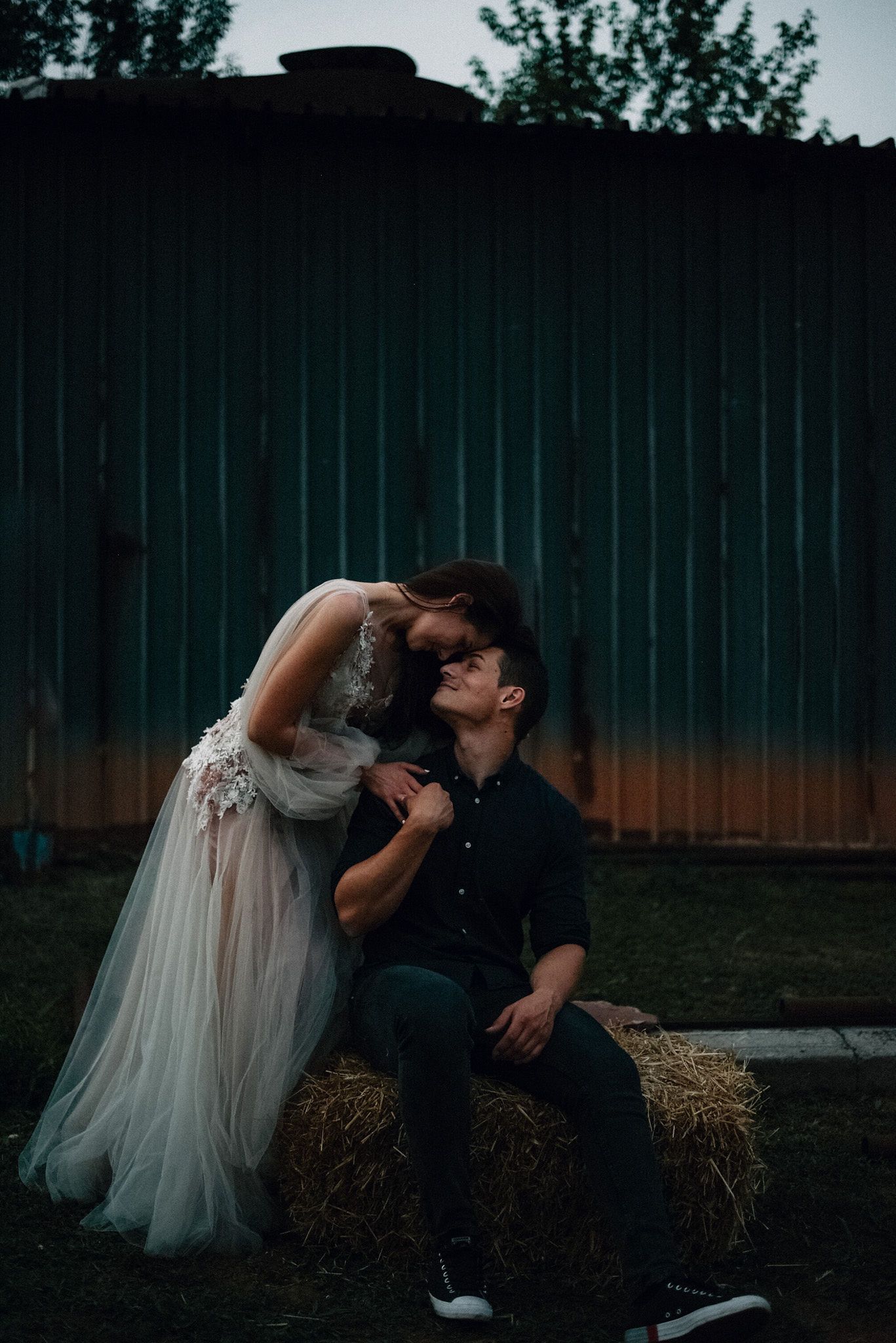 A couple shares tender moments while sitting on hay bales at dusk.