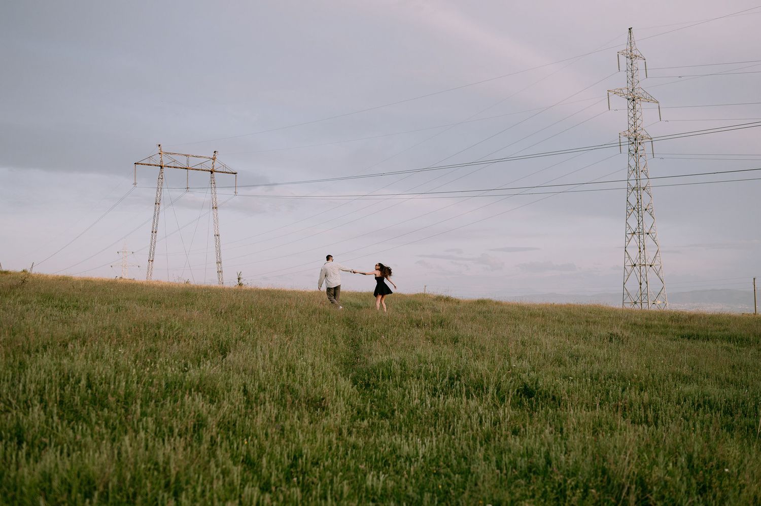 Electrical transmission towers stretch across rolling green hills with grazing cows visible in the distance.