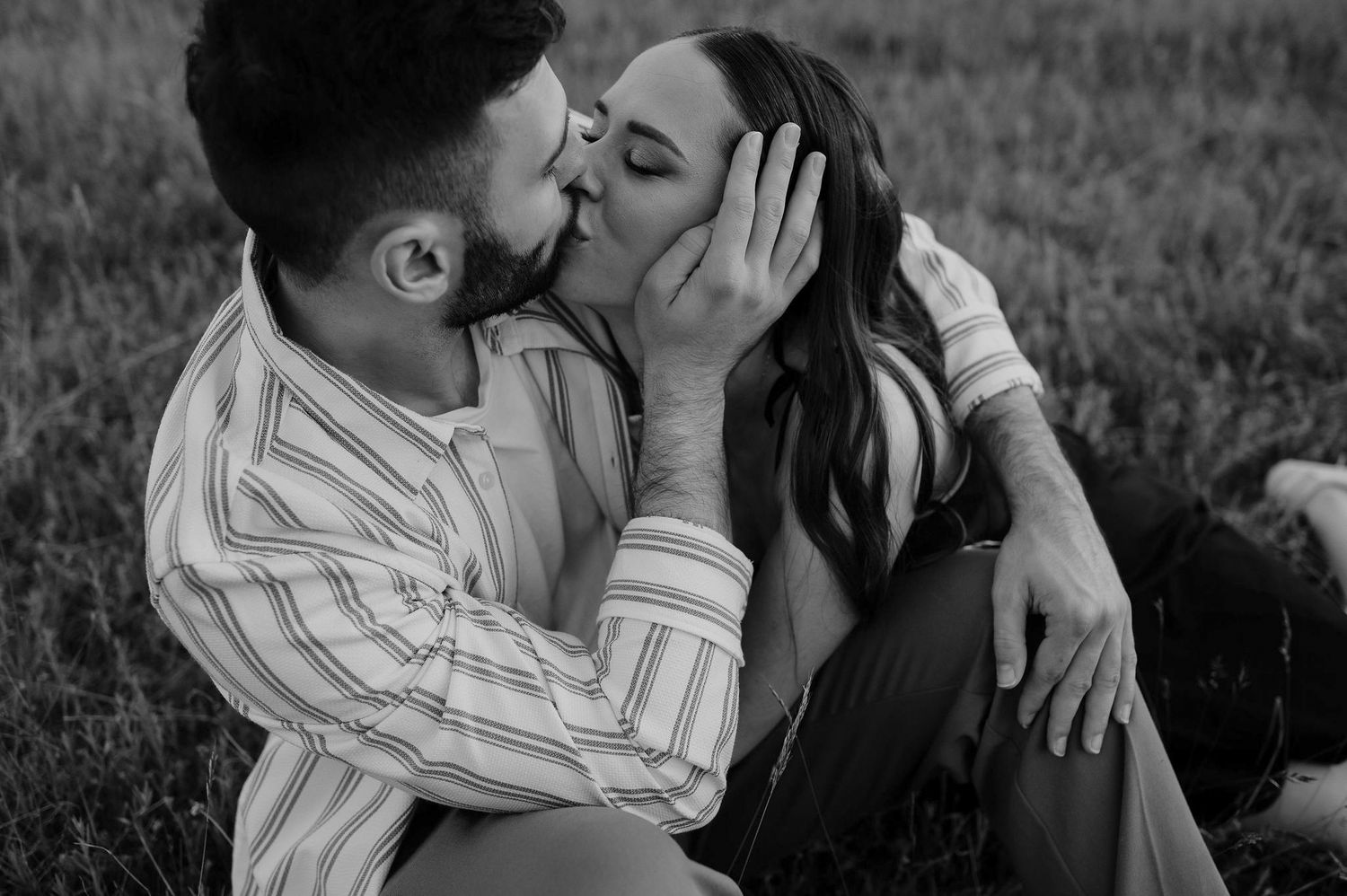 A romantic black and white photo series showing a couple sharing intimate moments in a grassy outdoor setting.