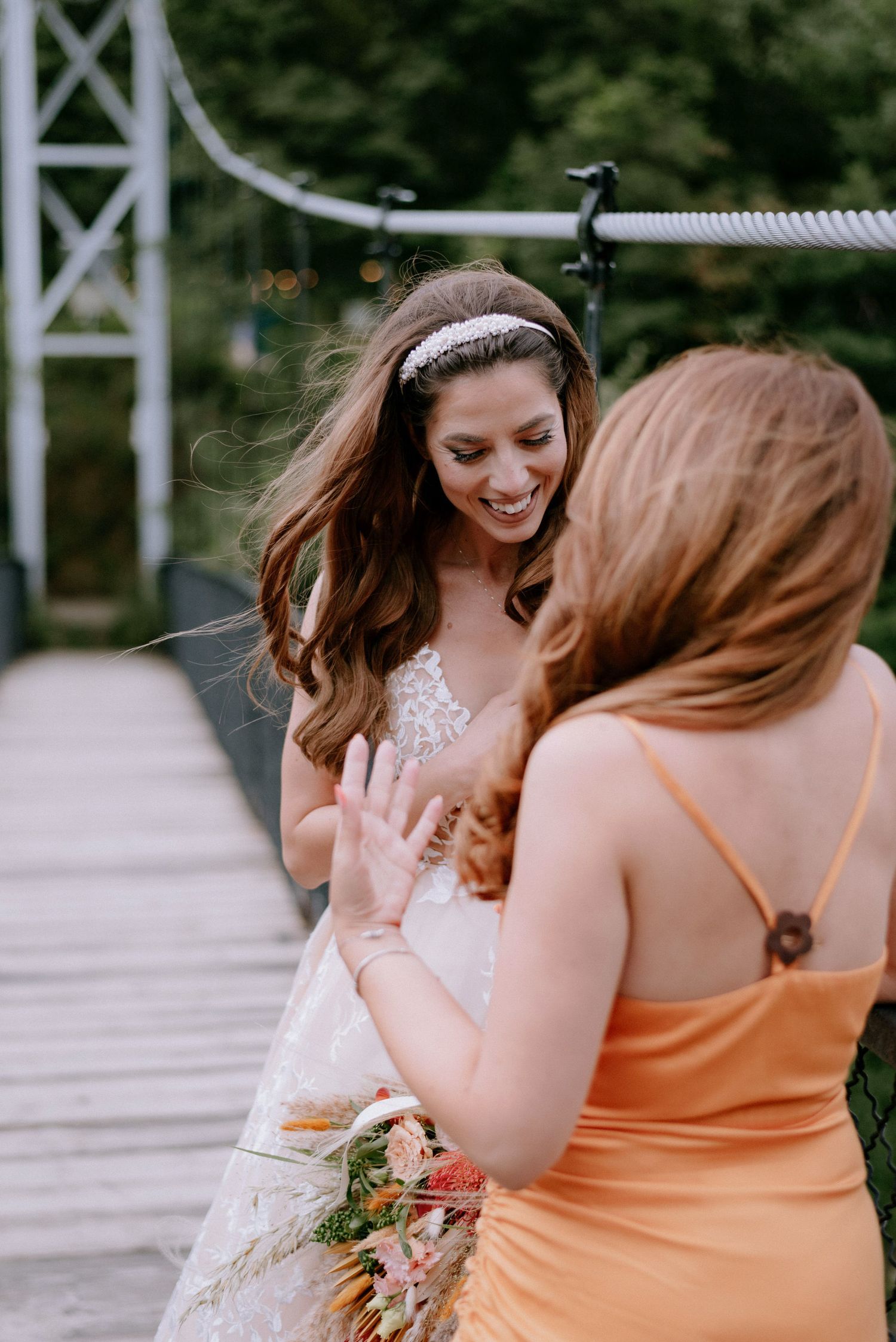 Two women in wedding attire share a candid laughing moment on a wooden deck.