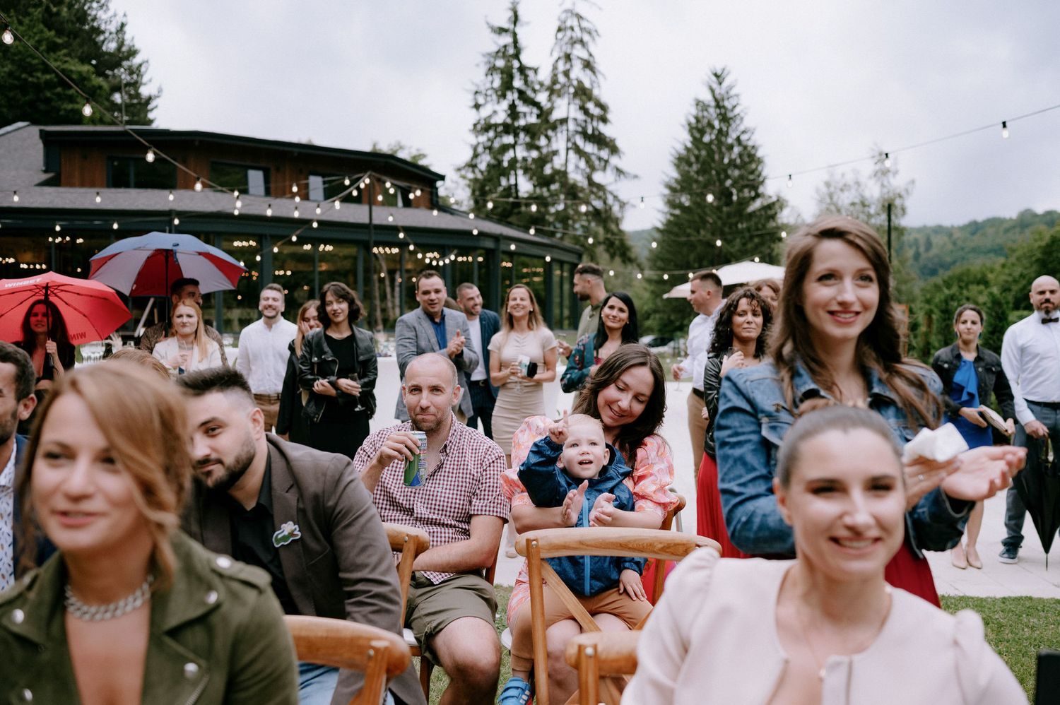 A group of people gather outdoors at picnic tables enjoying food and drinks during a summer celebration.