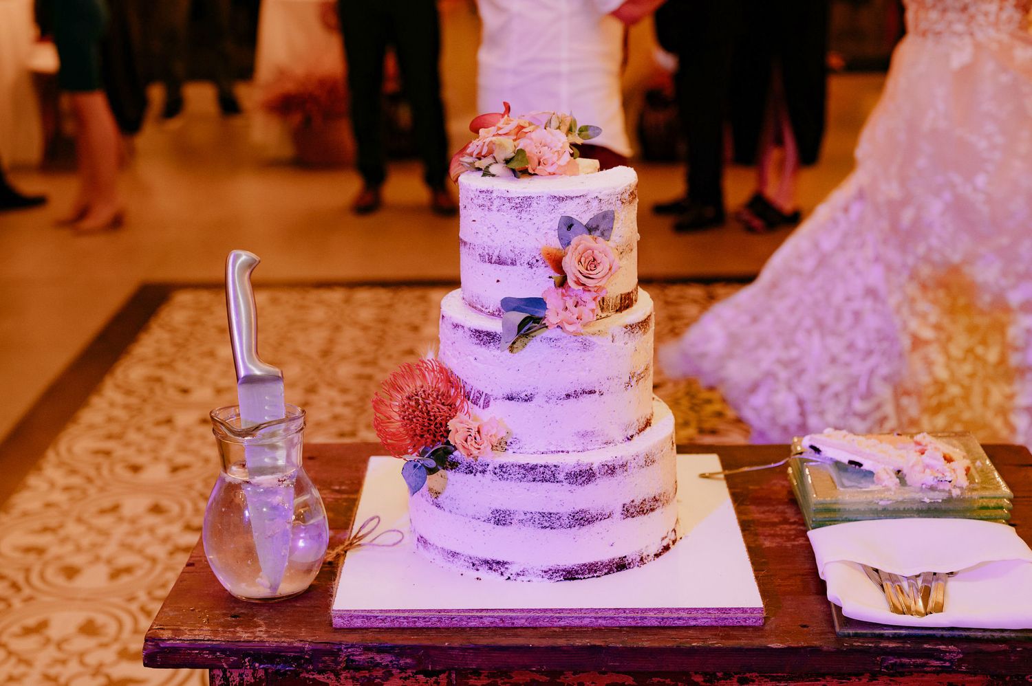 Elegant white wedding cake with delicate floral decorations and butterfly accents on display at a reception.