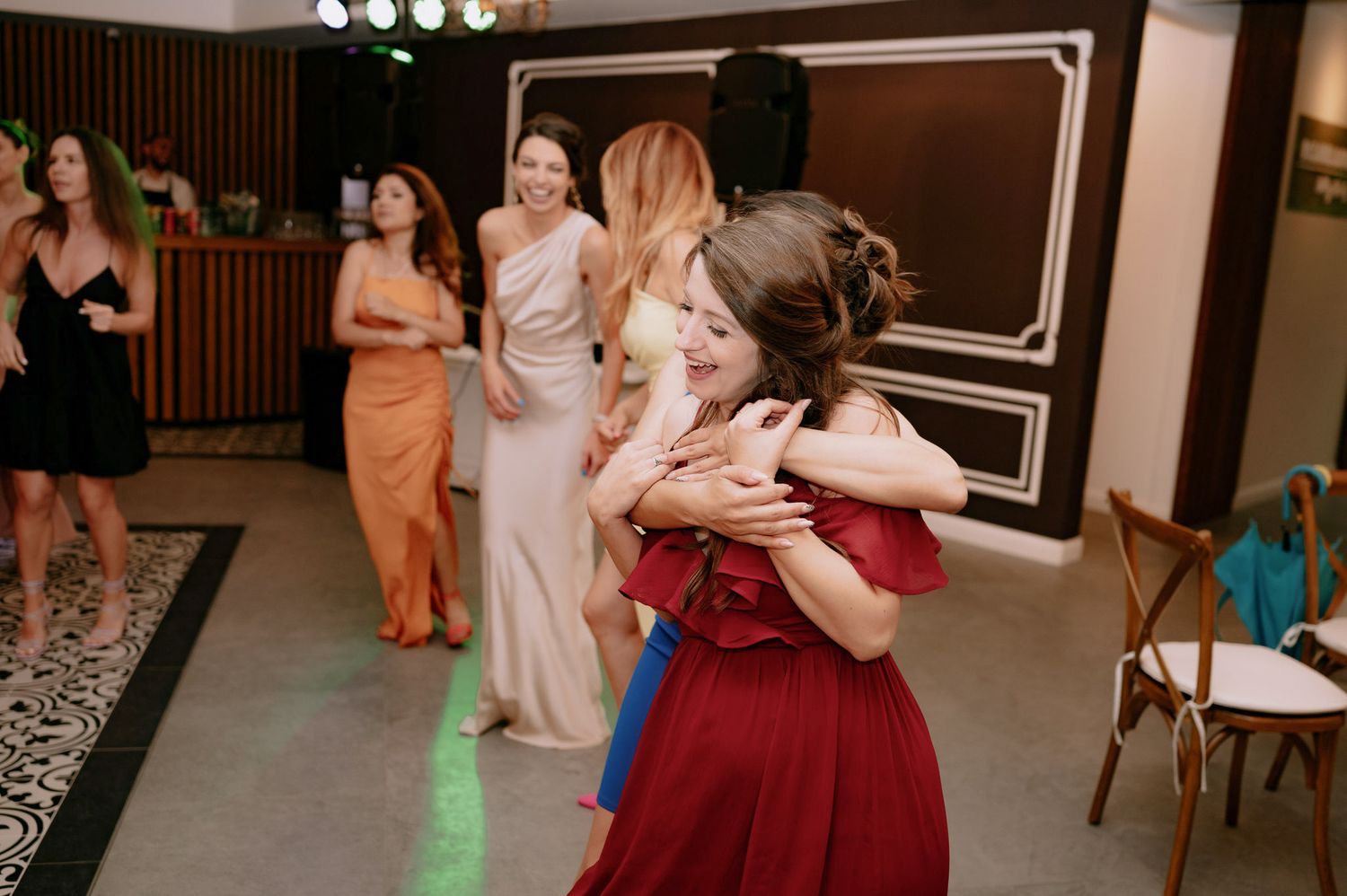People dance and celebrate at a wedding reception in a dimly lit venue with wood-paneled walls.