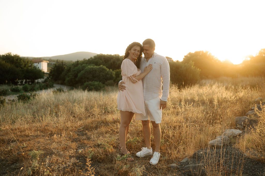A couple embraces in a golden sunset field with rolling hills in the background.