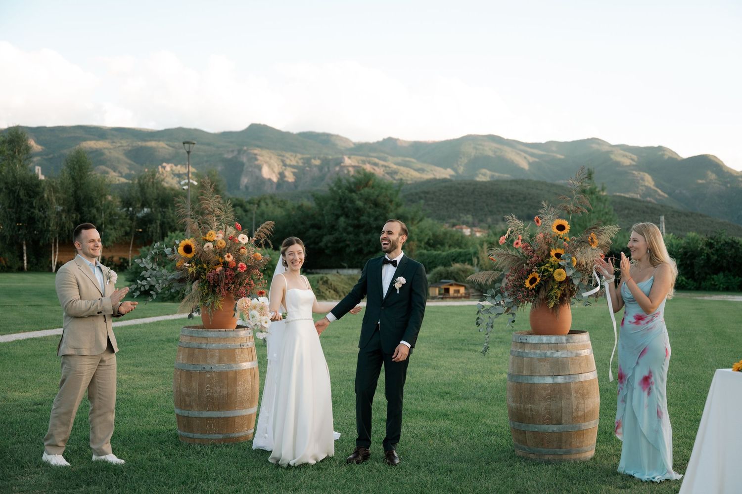 A wedding celebration on a lush golf course with wine barrels and floral arrangements against a mountain backdrop.
