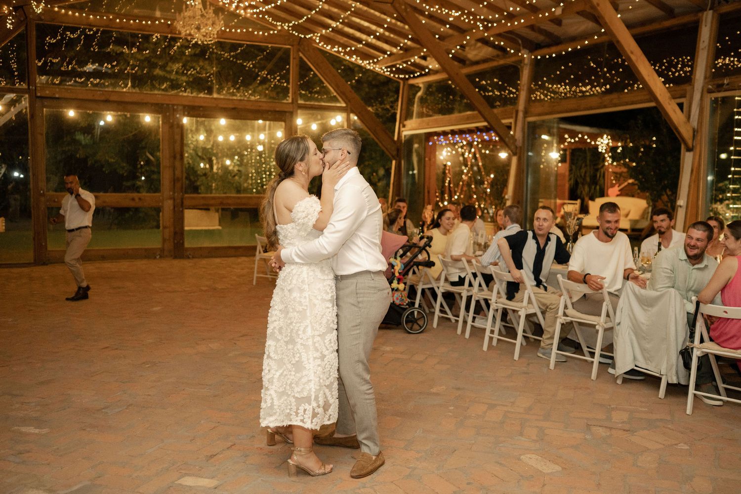 A romantic couple dances together on an outdoor patio under warm string lights at an evening wedding reception.