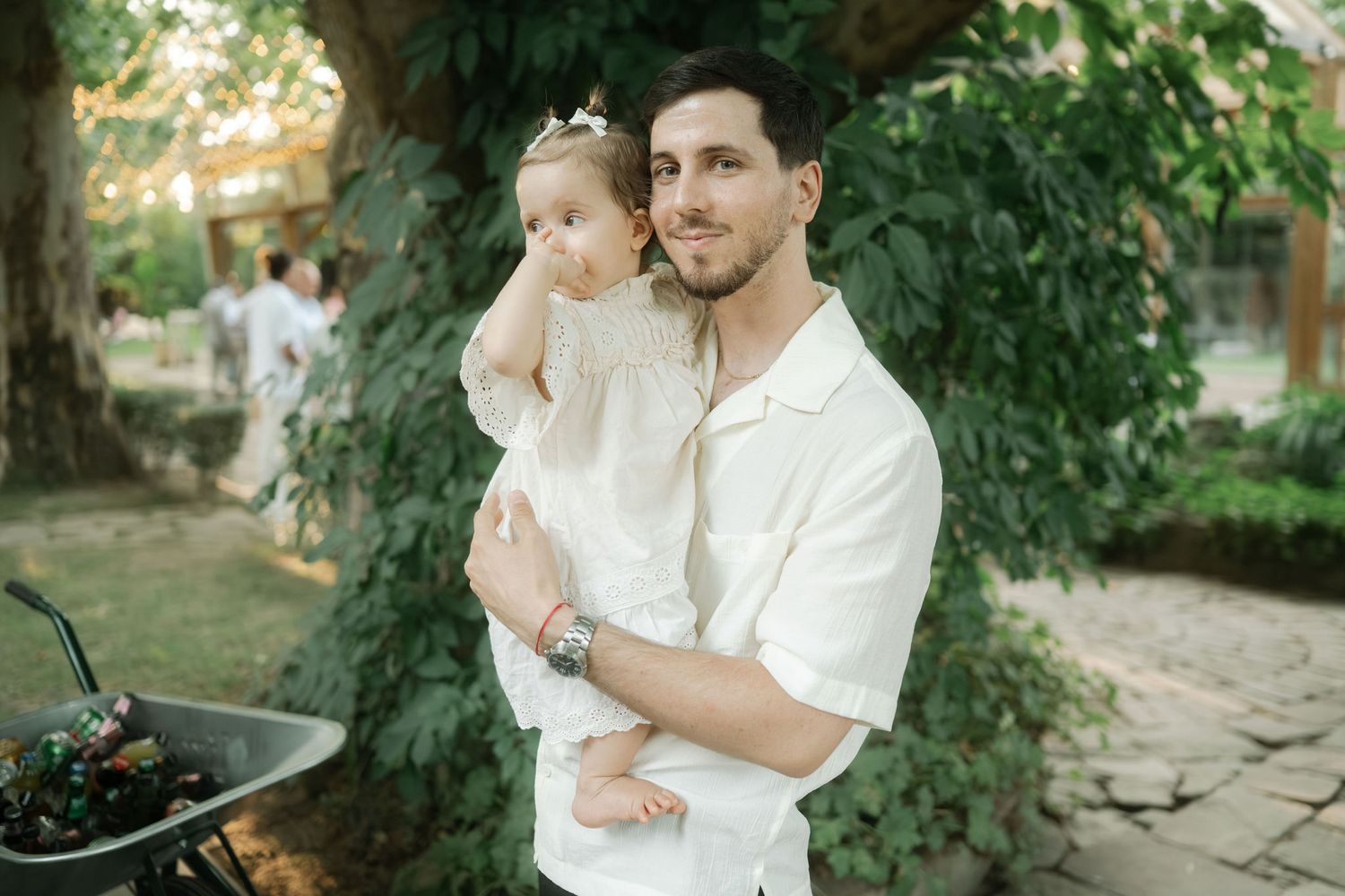 A couple in white outfits embraces in a romantic outdoor garden setting during a golden hour photoshoot.