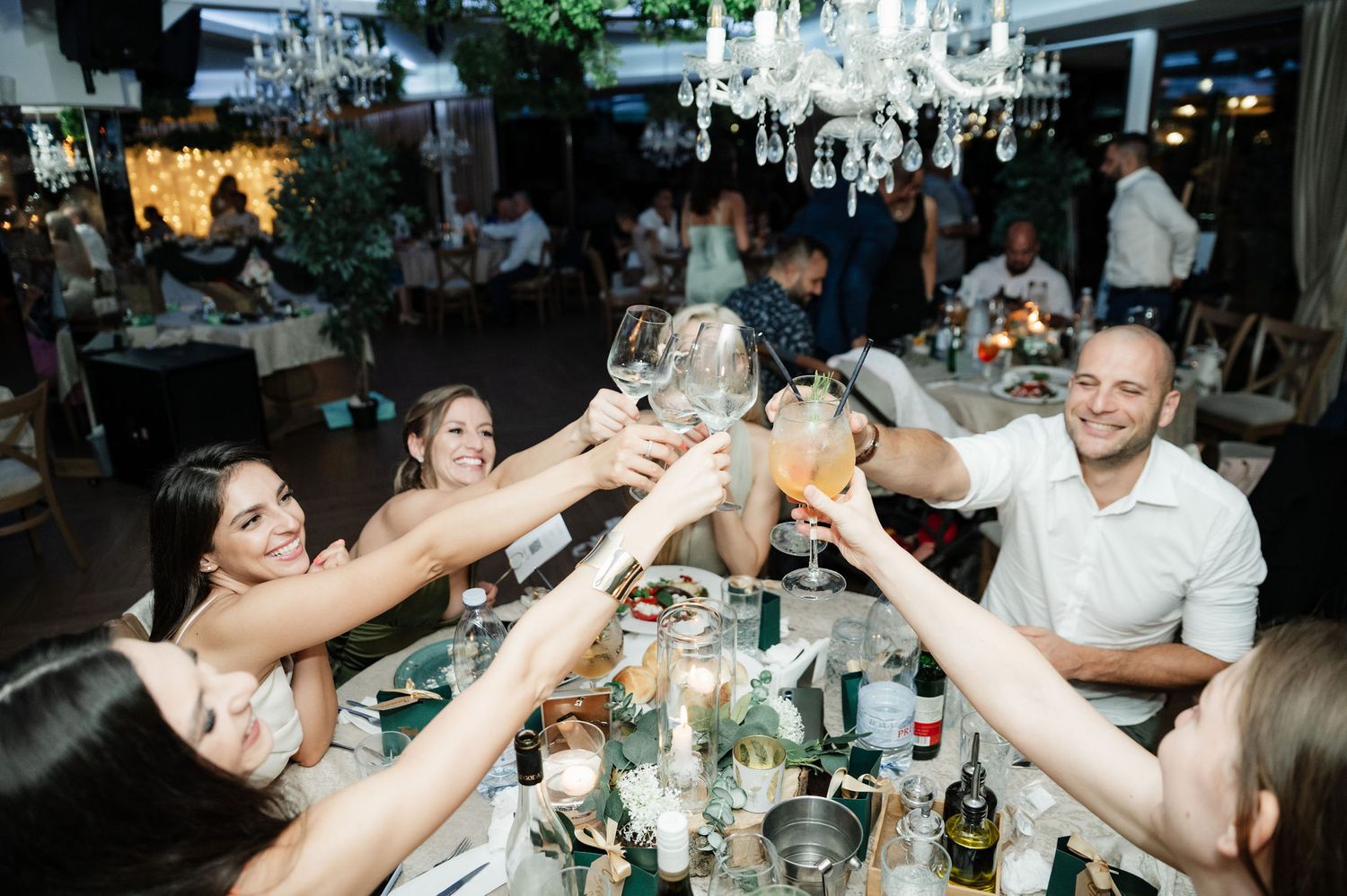 People dancing and celebrating at a lively reception party under elegant chandeliers.