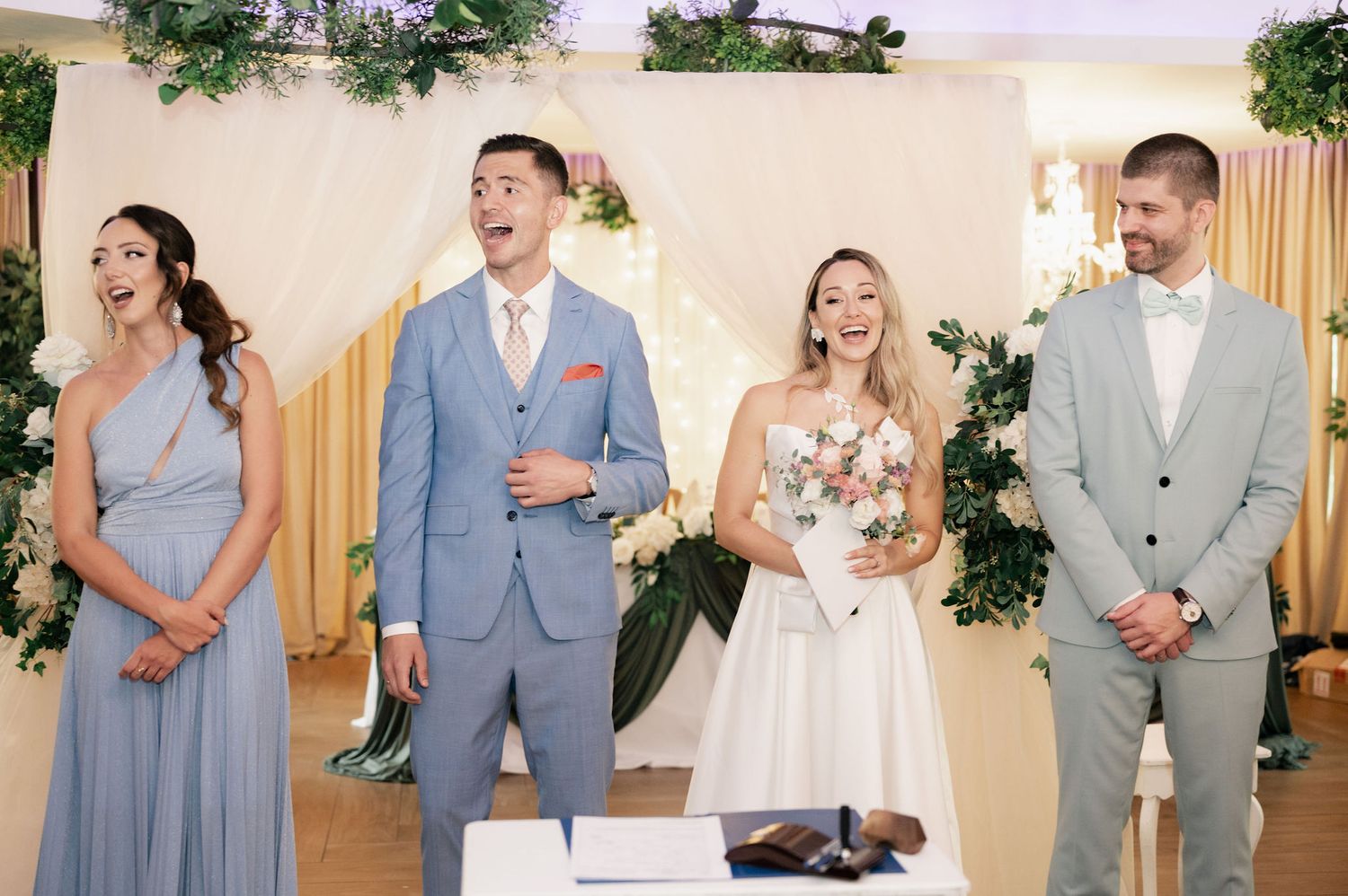 Wedding party members in light blue and gray attire pose for photos during a celebration.