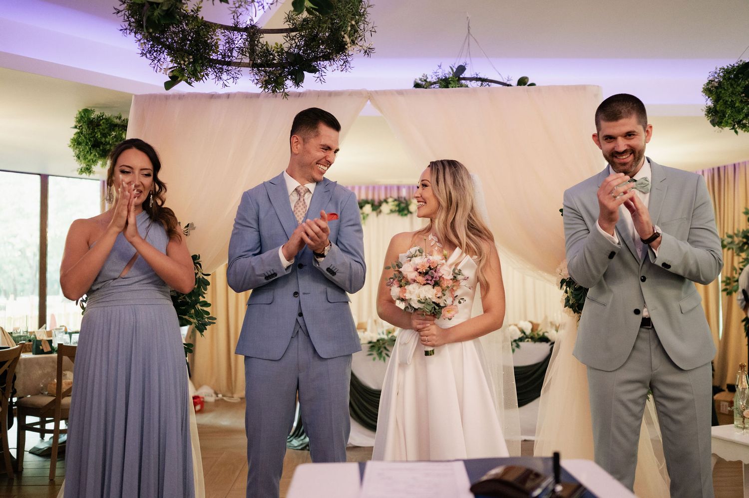 Wedding party in gray and white attire stands together during formal ceremony at indoor venue.