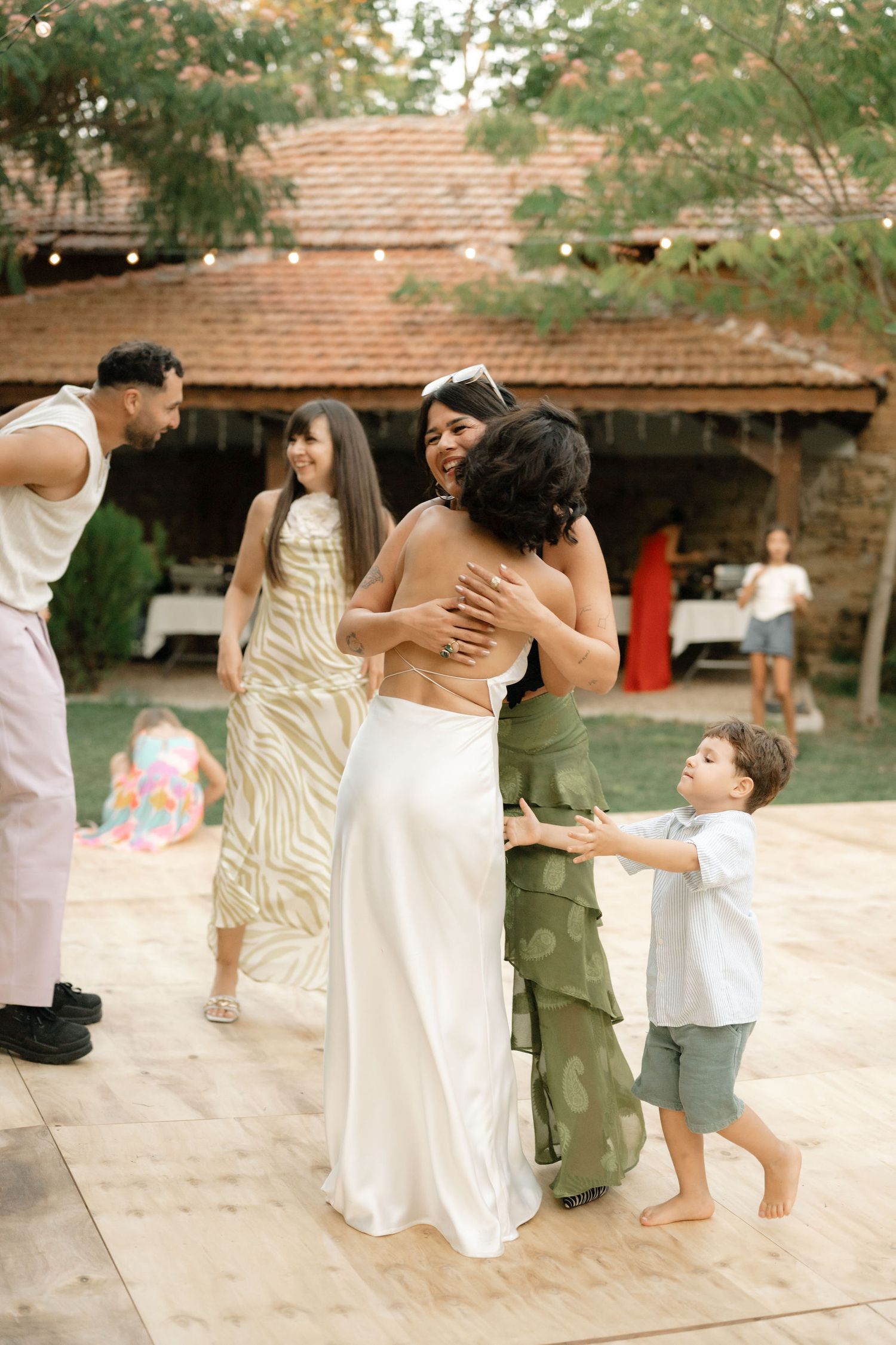A group of people dancing together in white dresses and casual attire on an outdoor patio.