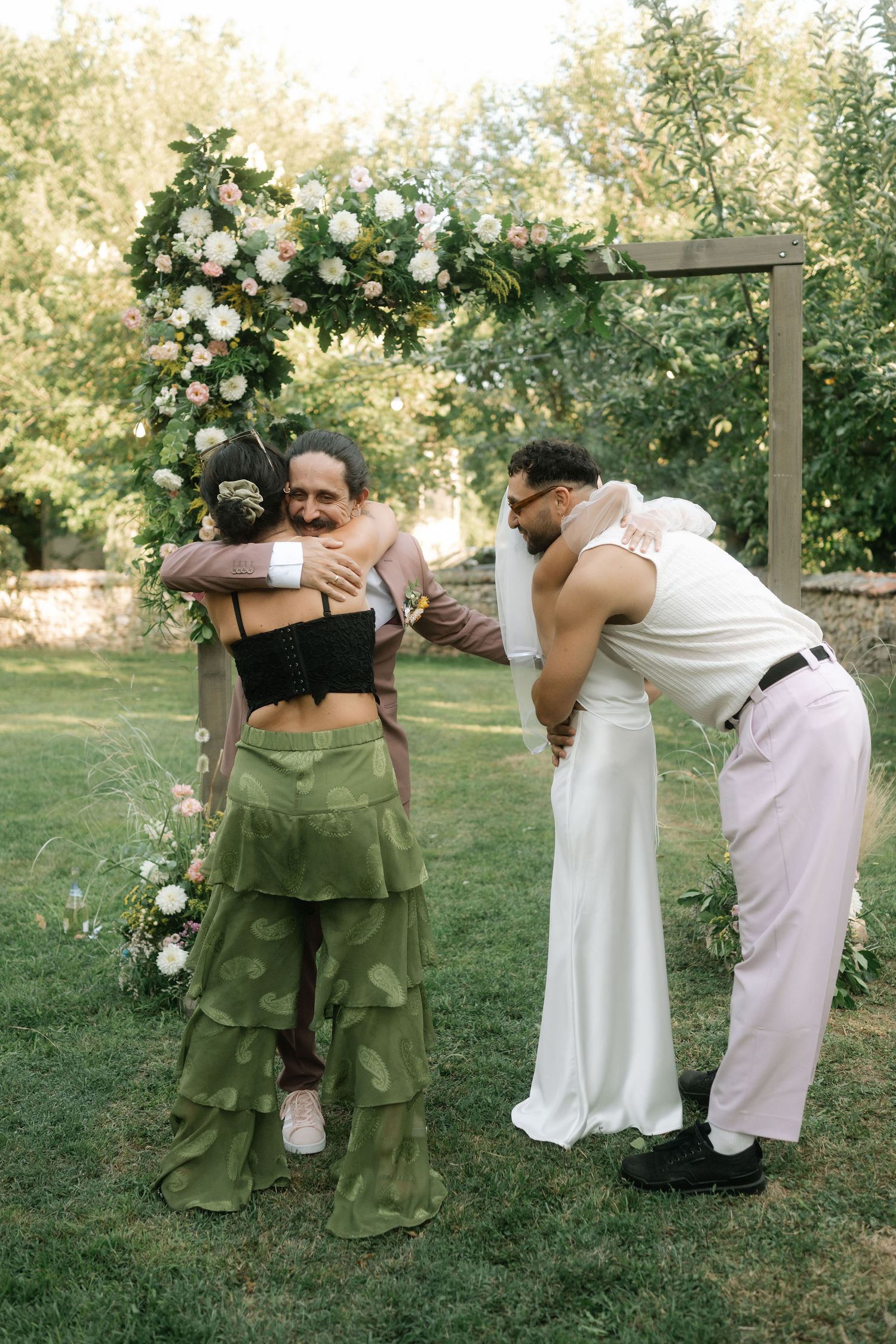 Wedding party poses playfully in sequence of candid moments by floral arch in outdoor garden setting.