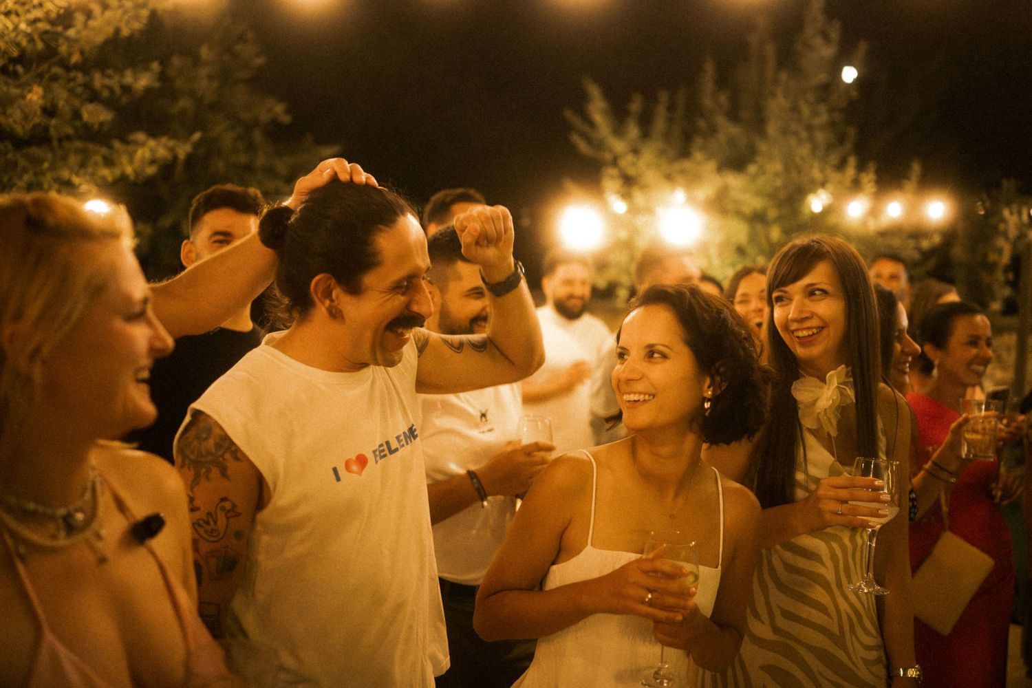 Friends gathered at a nighttime celebration with string lights illuminating their joyful interactions.