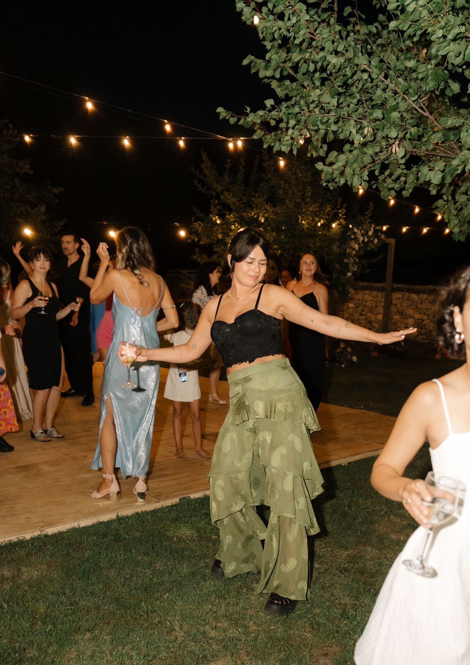 People dancing outdoors at night under string lights and trees during what appears to be a festive celebration.
