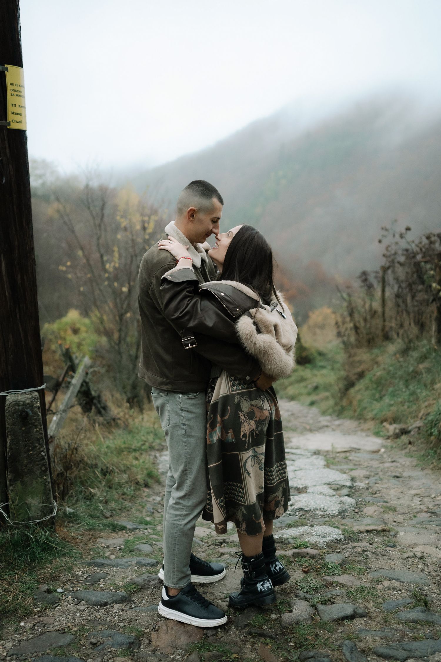 A couple shares a romantic moment on a misty mountain trail during autumn.