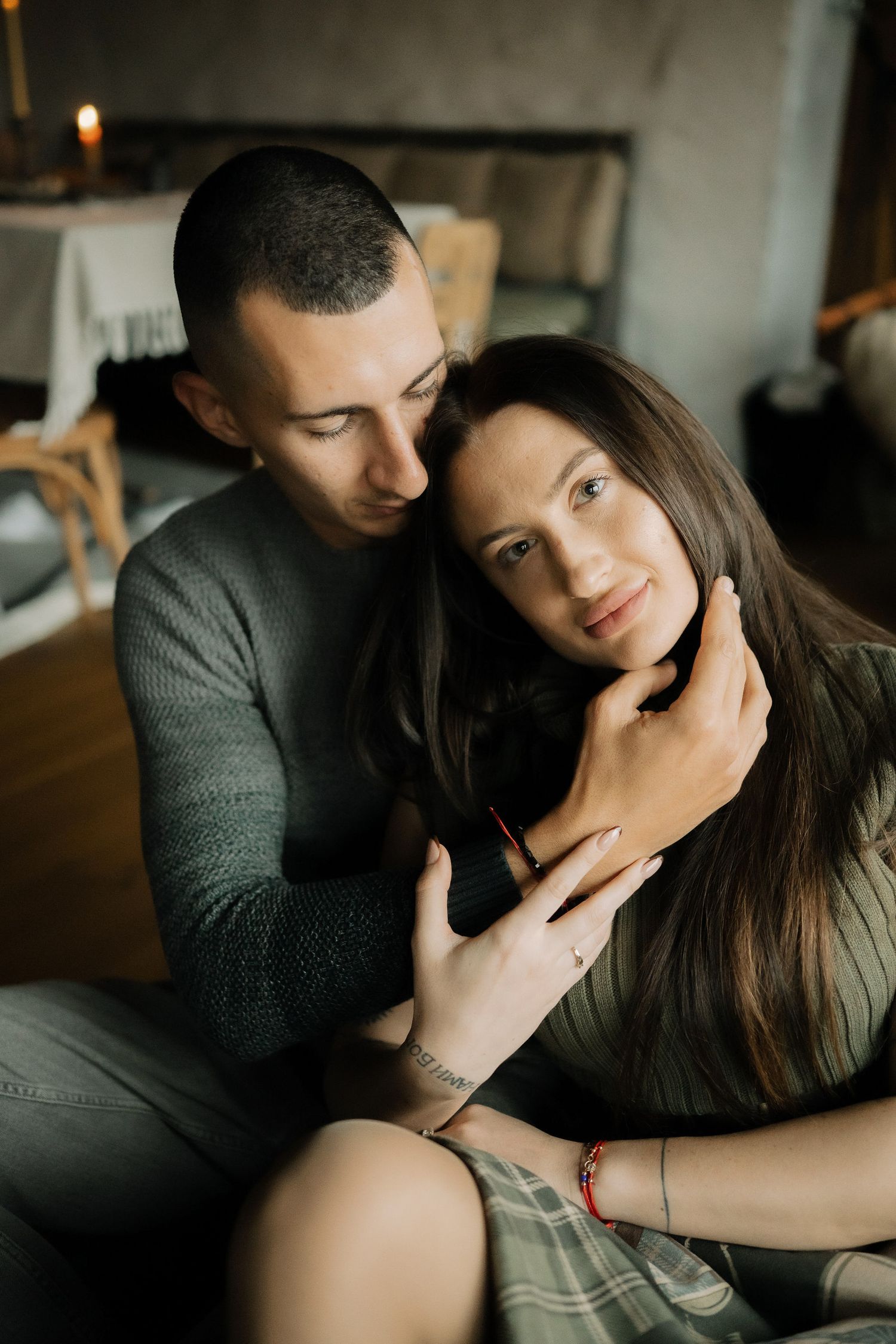 Intimate couple shares tender moments in moody indoor photoshoot with warm lighting and romantic atmosphere.