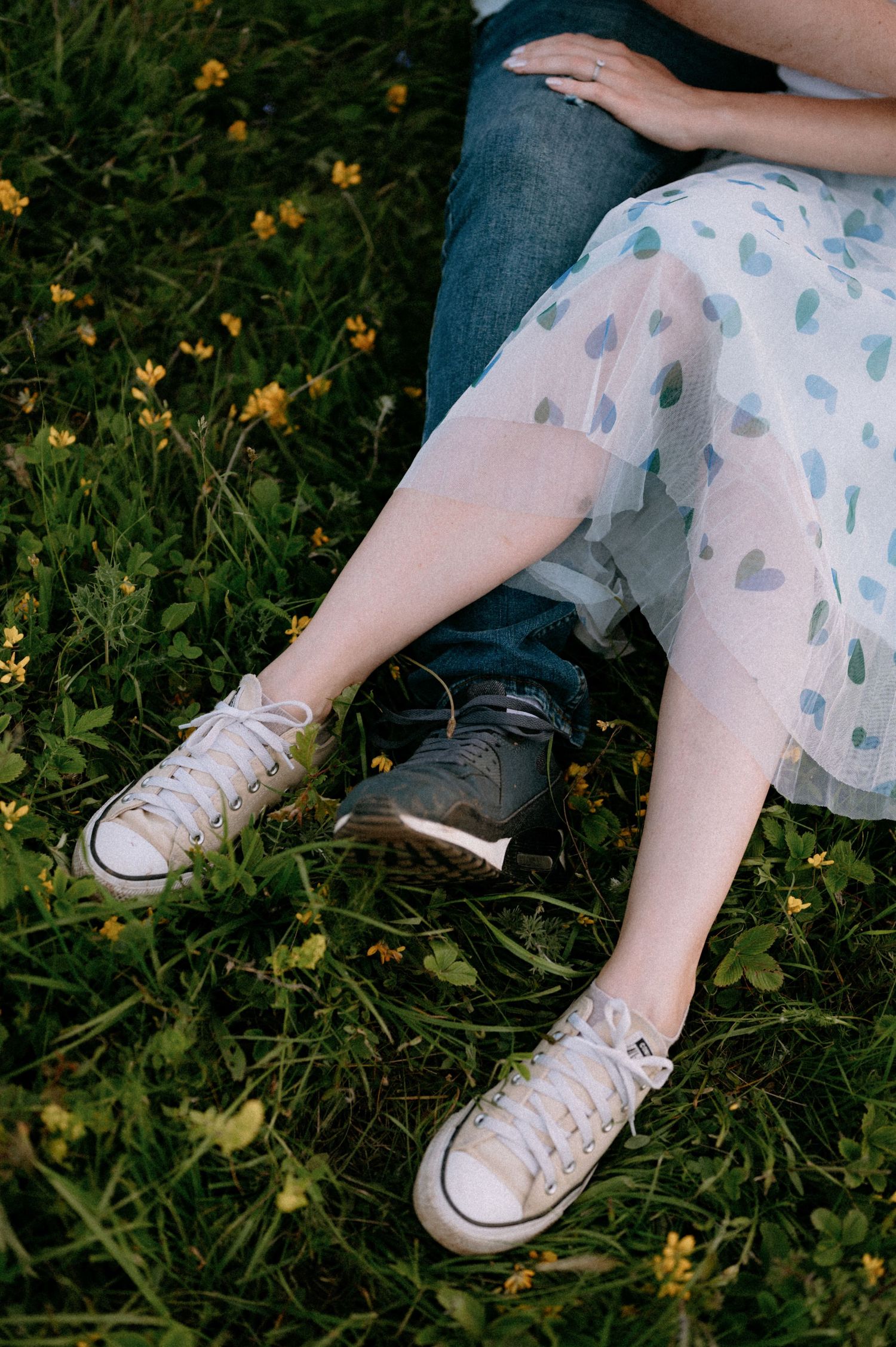 Close-up of couple's feet and heart-patterned blanket amid mountain wildflowers.