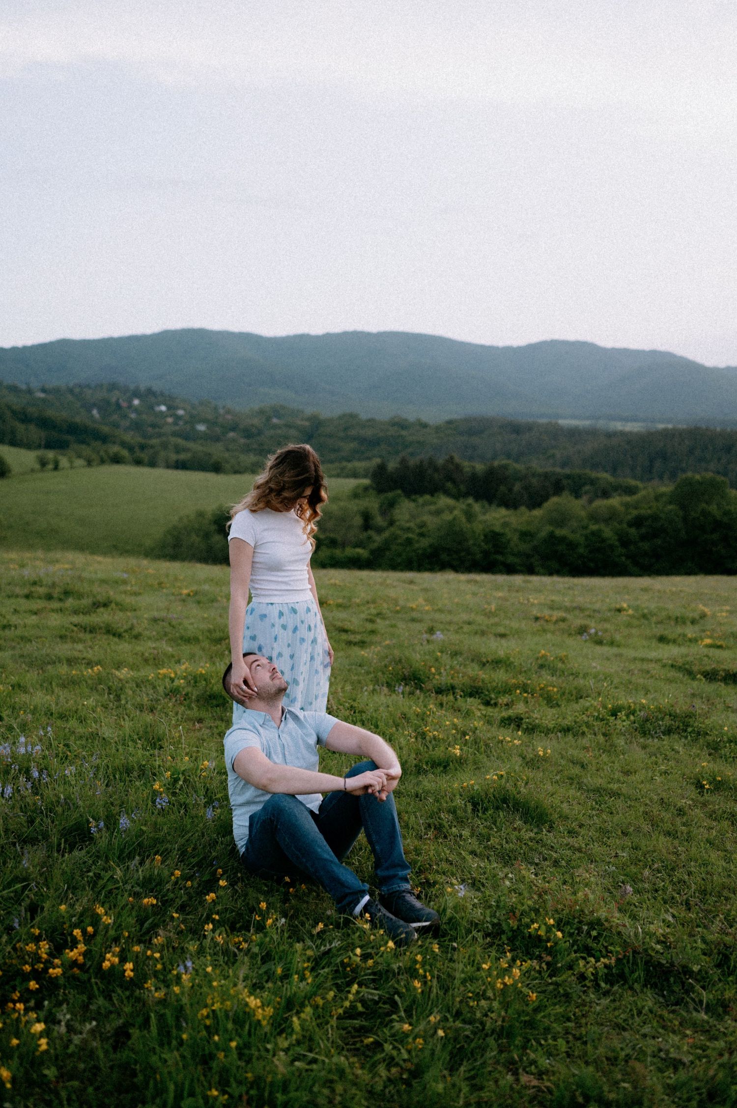 A couple shares a tender embrace while sitting in a mountain meadow at dusk.