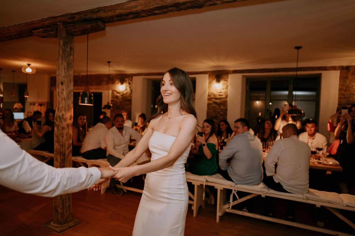 Wedding guests watch as a couple performs their first dance in a rustic reception venue.