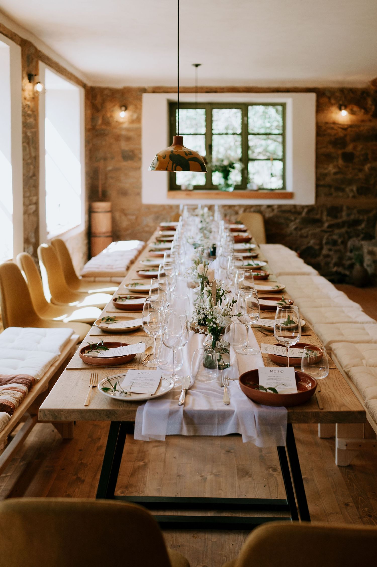 Rustic dining room with long wooden tables set for formal dining with white table runners.