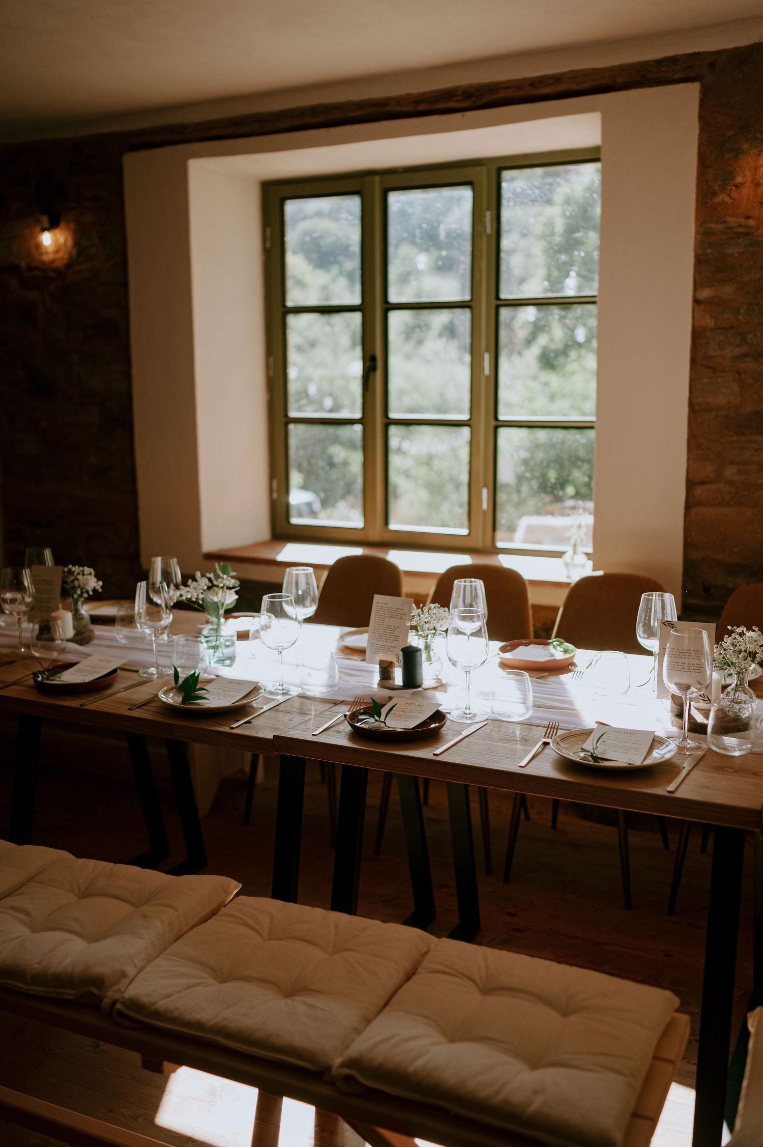 Formal dining table setup near large window in stone-walled room with natural lighting.