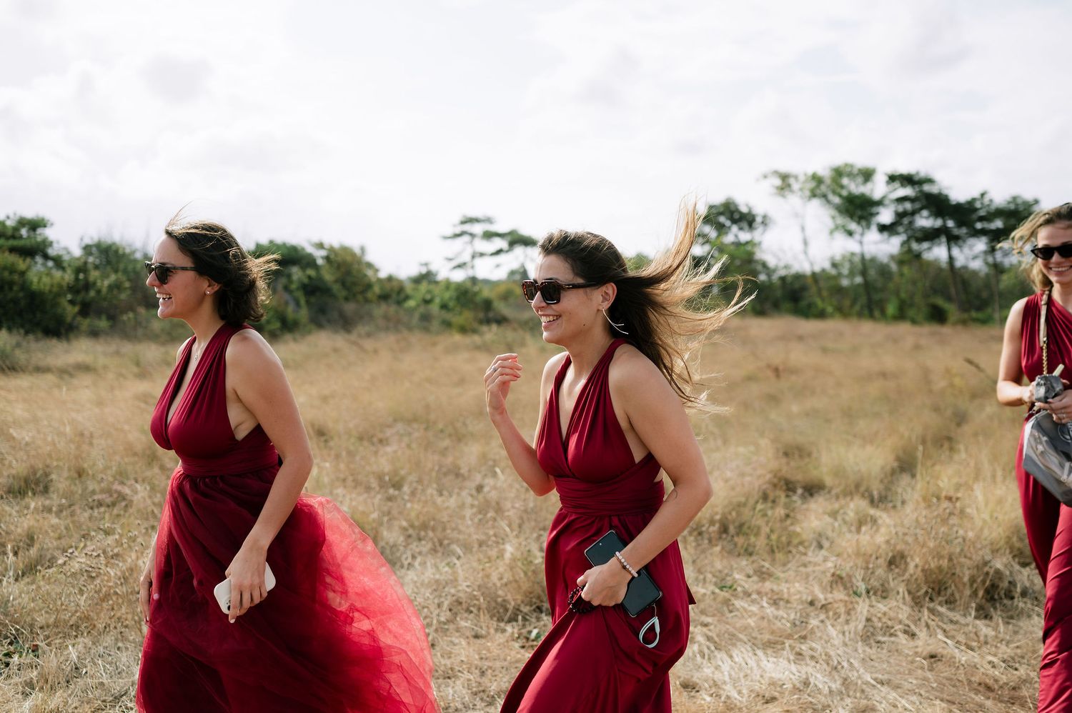 Group of bridesmaids in burgundy dresses walking along a scenic outdoor path.
