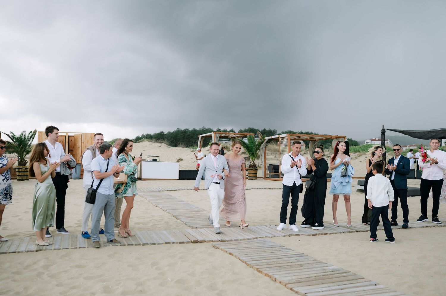 Panoramic view of a beach wedding ceremony with wooden walkway and guests in attendance.