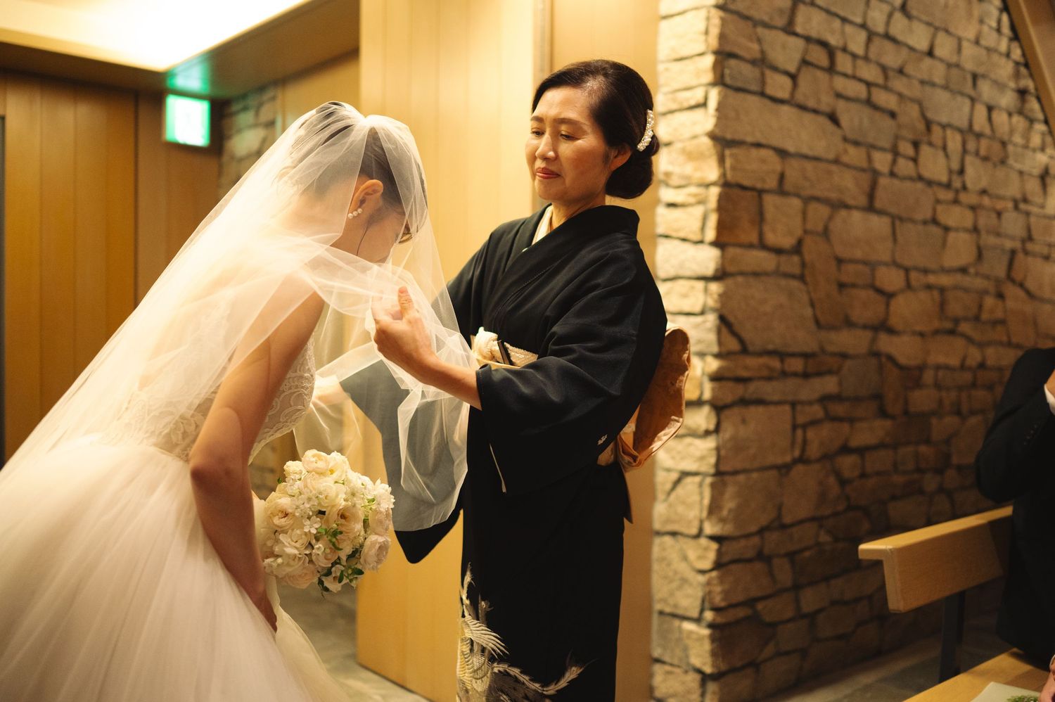 Tender greeting between bride and guest in elegant stone-walled hallway.