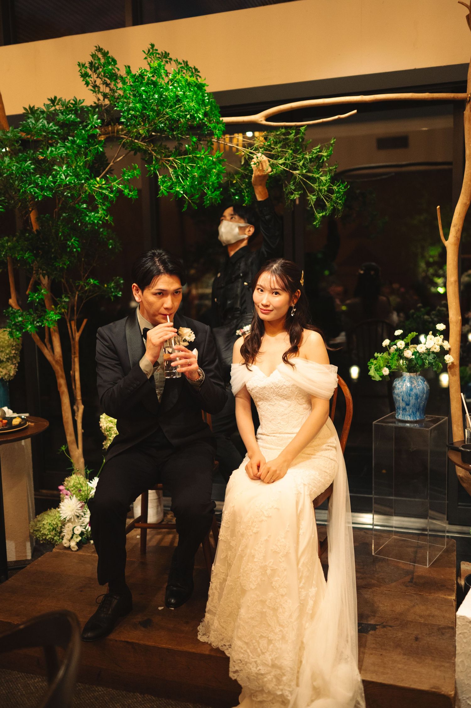A couple sits beneath illuminated green trees during their wedding reception.