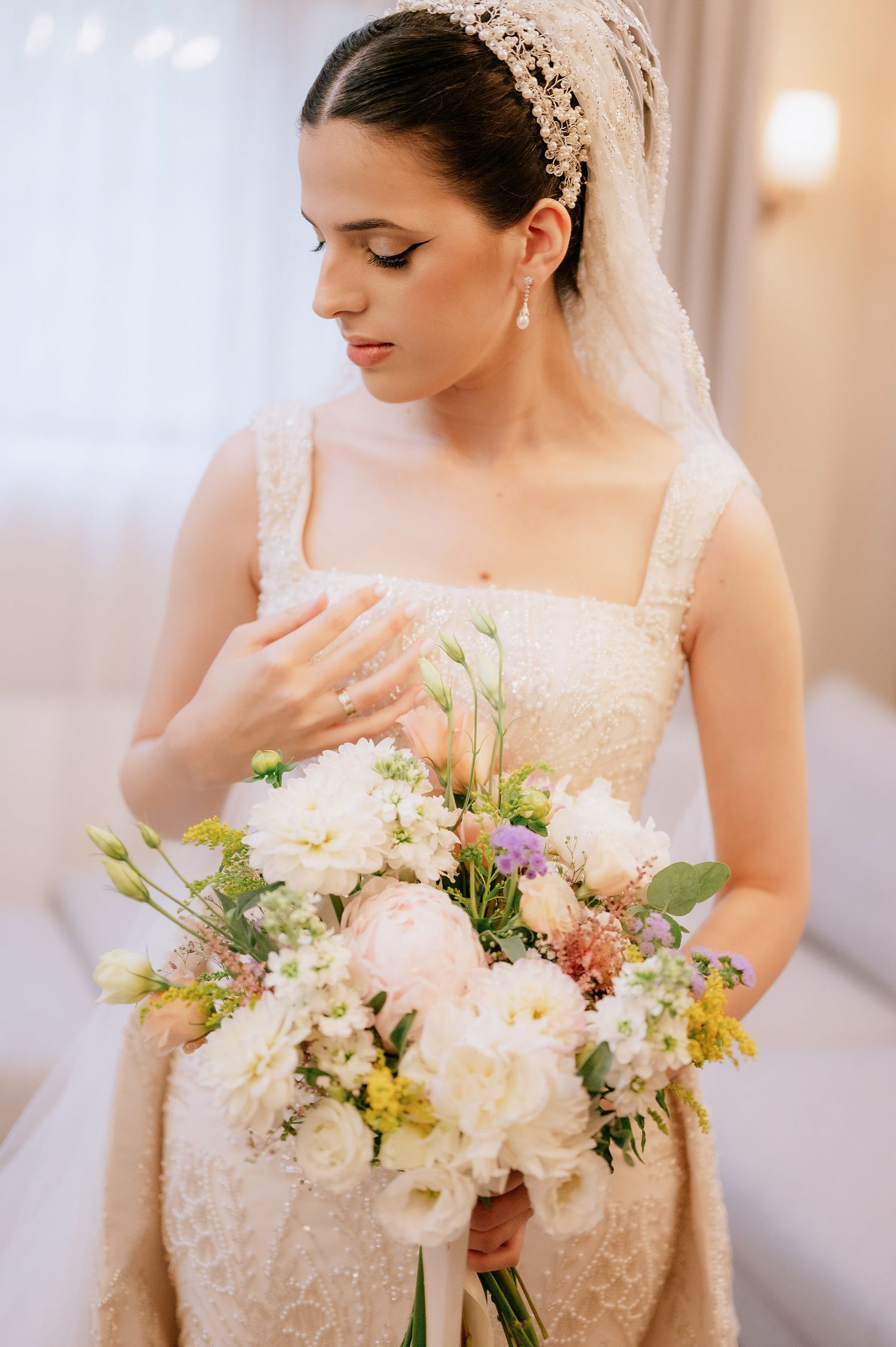 Bride in lace dress holds beautiful pastel bouquet with white and yellow flowers.