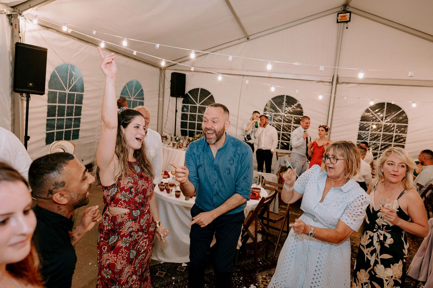 Wedding party dances and celebrates in a beautifully lit tent venue.